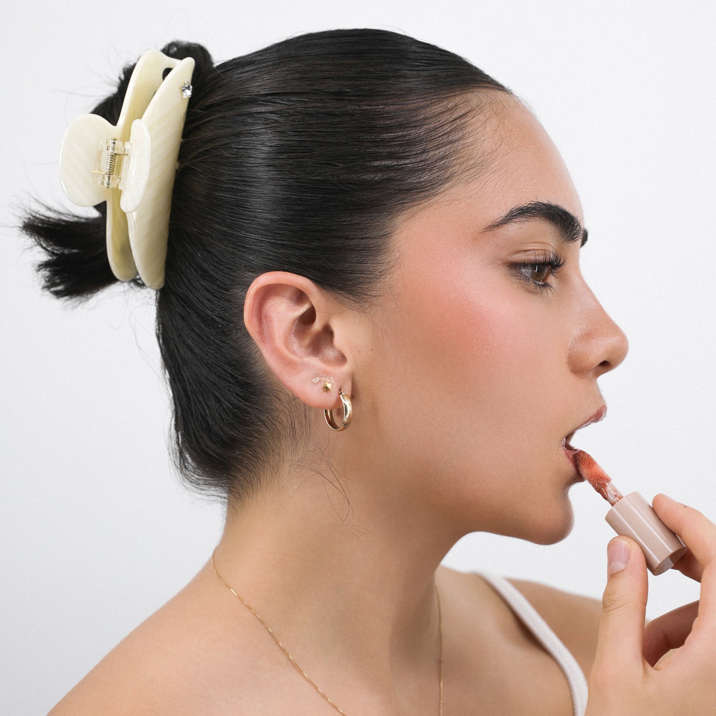 Woman applying lipstick and wearing Luna Wave white ivory pearl hair claw clip with a white background