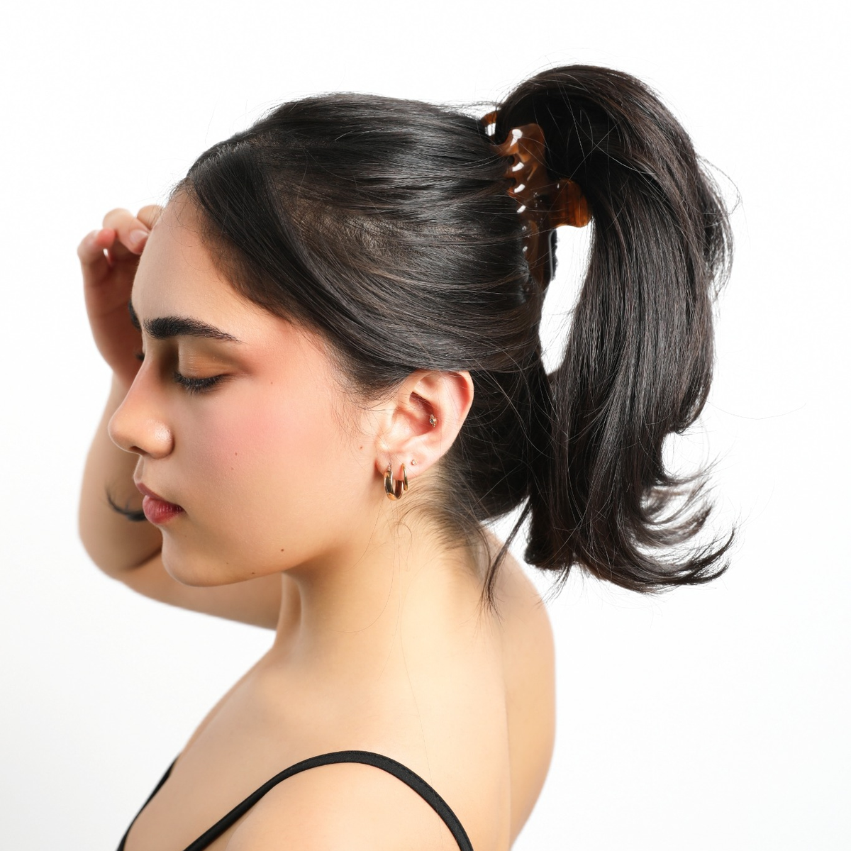 Model wearing the brown Luna Wave Jelly Claw in Amber in a high ponytail, with her hand near her forehead.