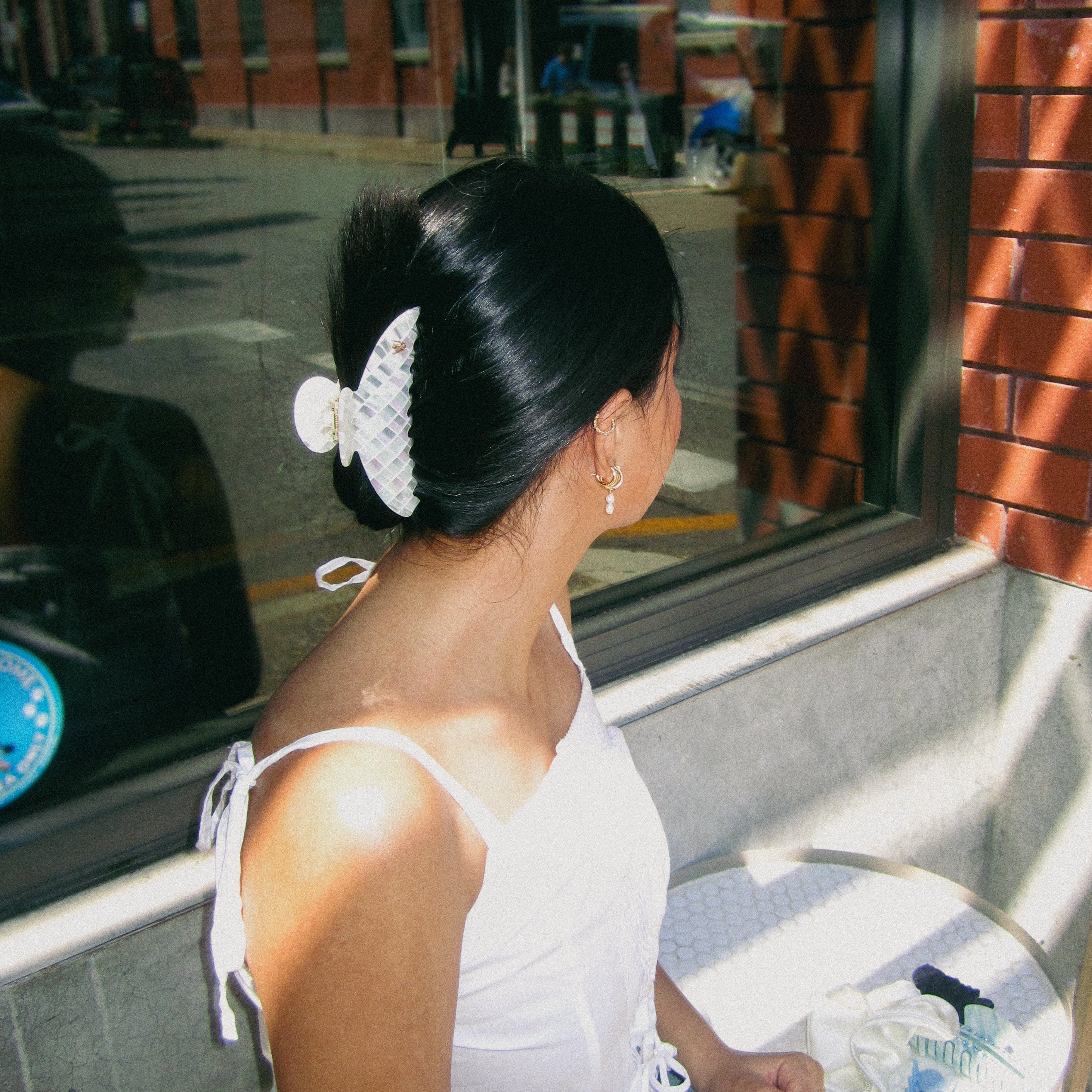 Luna Wave model wearing a opal claw clip, styled in a low bun while sitting outdoors in the city