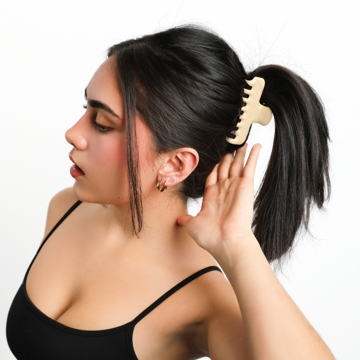 Three quarter view of a model wearing Luna Wave Jelly Claw in Butter in a high ponytail, with her hand beside her ear.