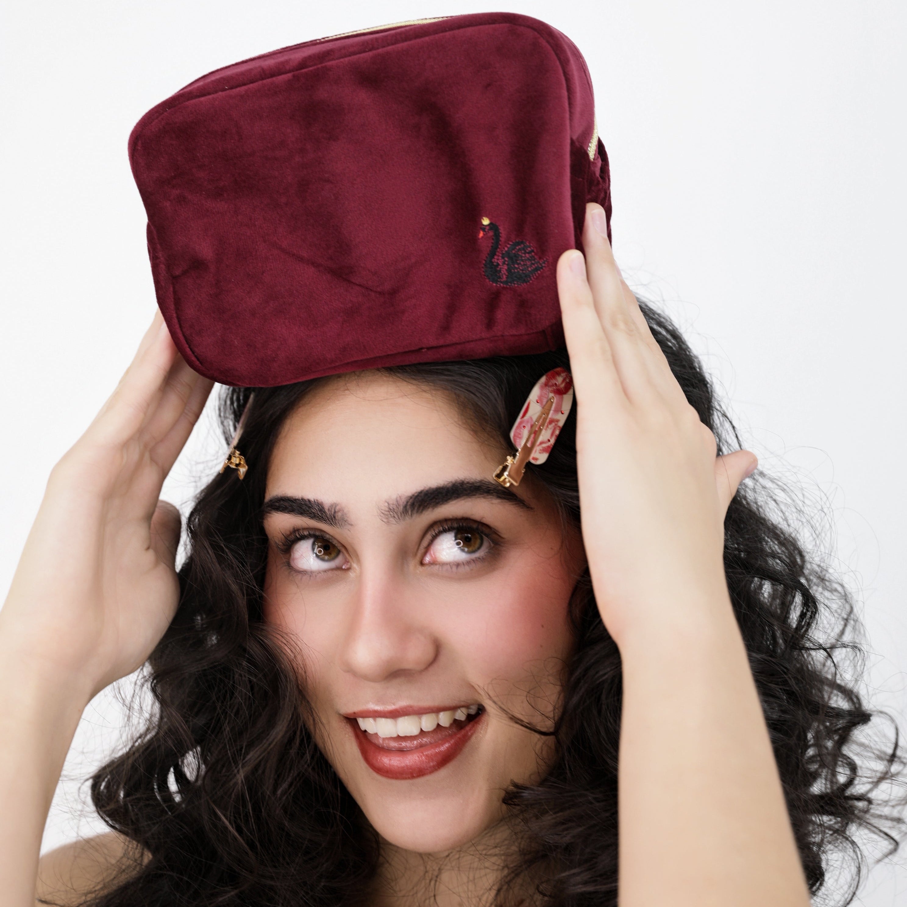 Woman holding a Luna Wave red velvet odette cosmetic pouch bag above her head against a white background