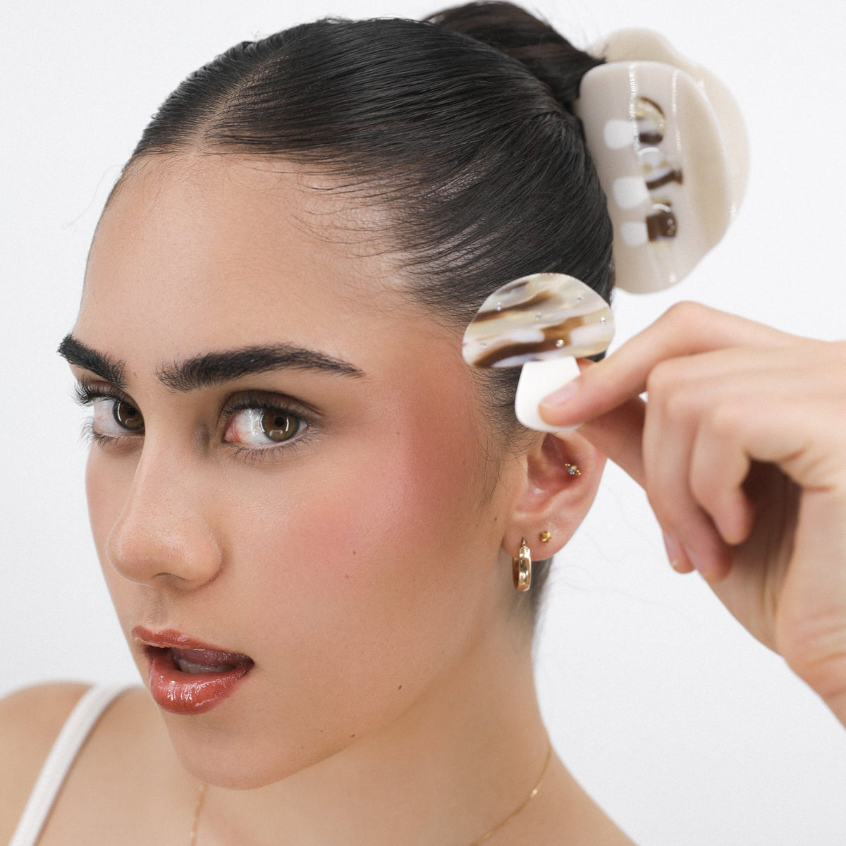 Woman holding a Luna Wave brown creamy hair clip against her ear with a plain background
