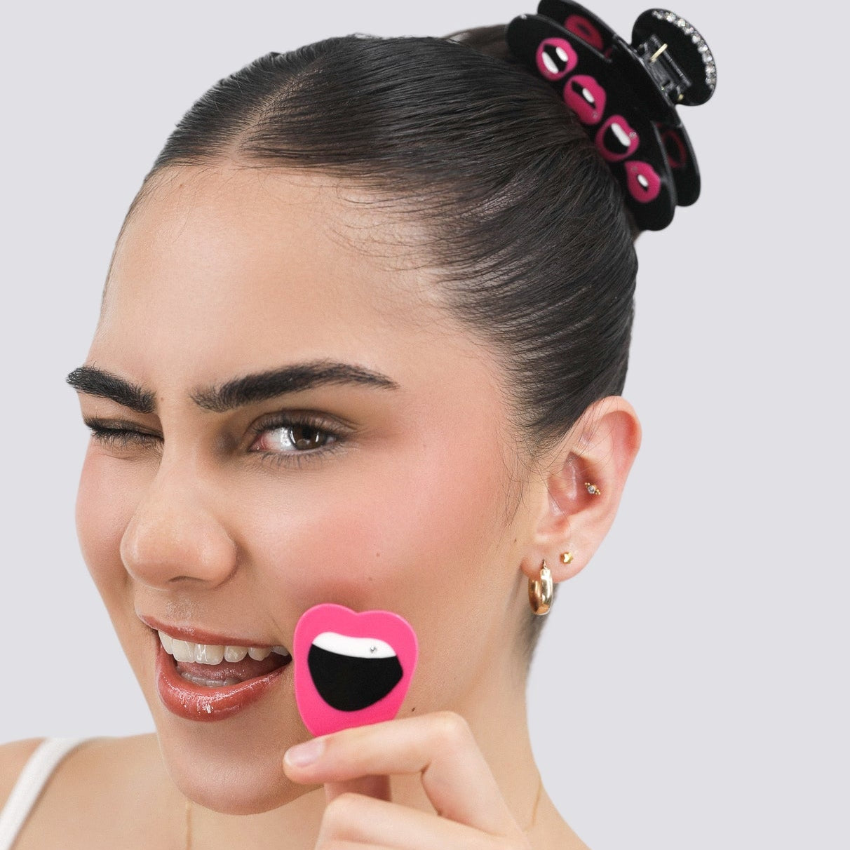 Woman holding a Luna Wave aria hair clip with a smiley face on it against a white background