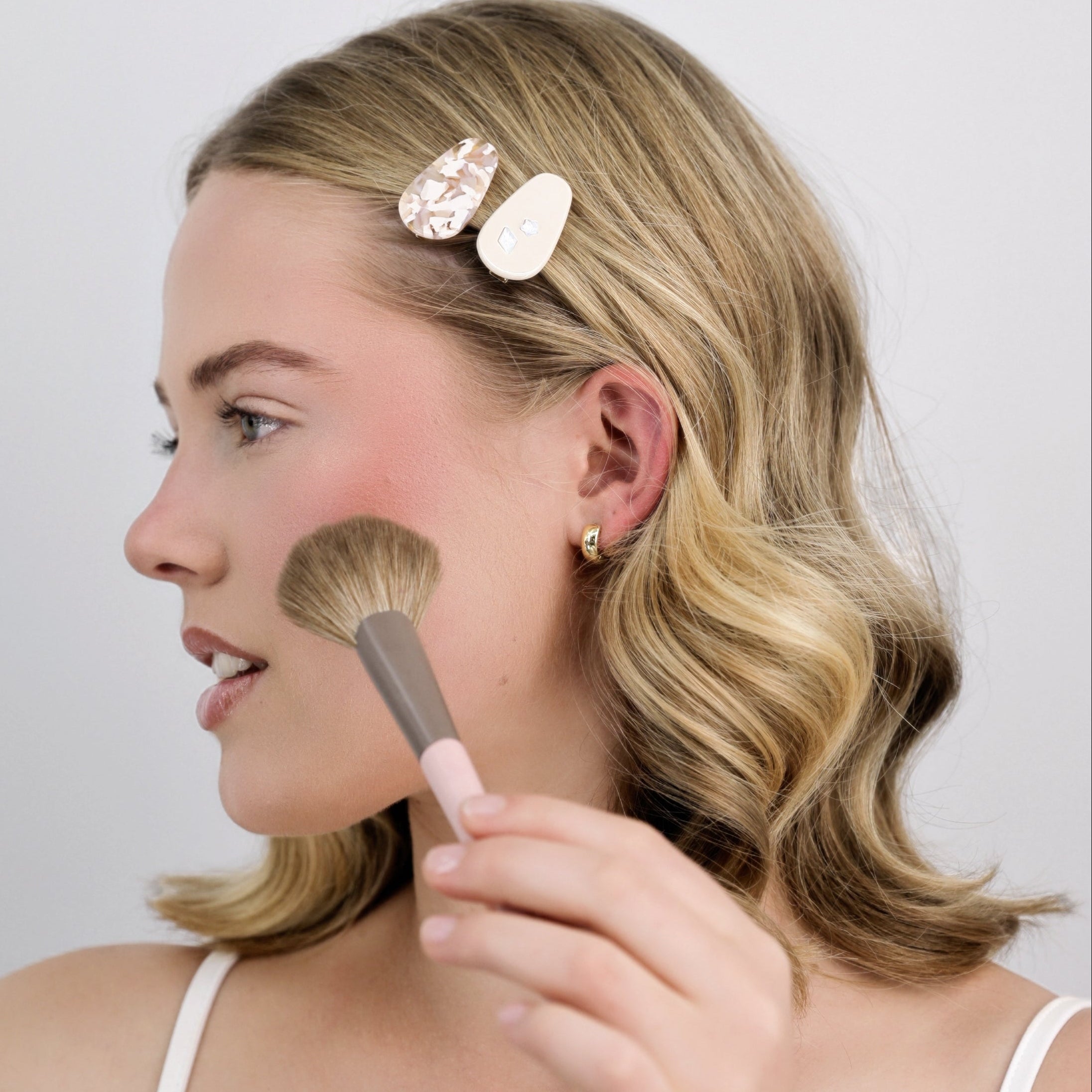 Woman applying makeup with Luna Wave pink coffee petite hair clips on a plain background