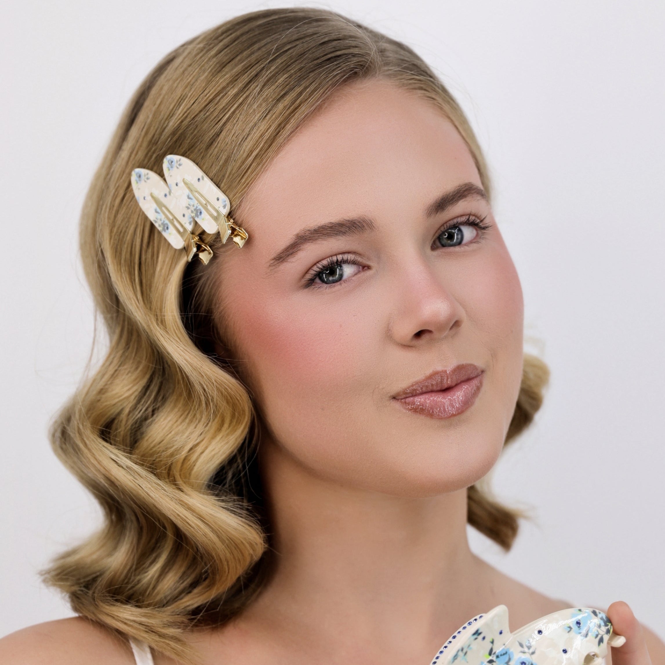Woman with styled hair holding a Luna Wave white day garden hair clips against a plain background