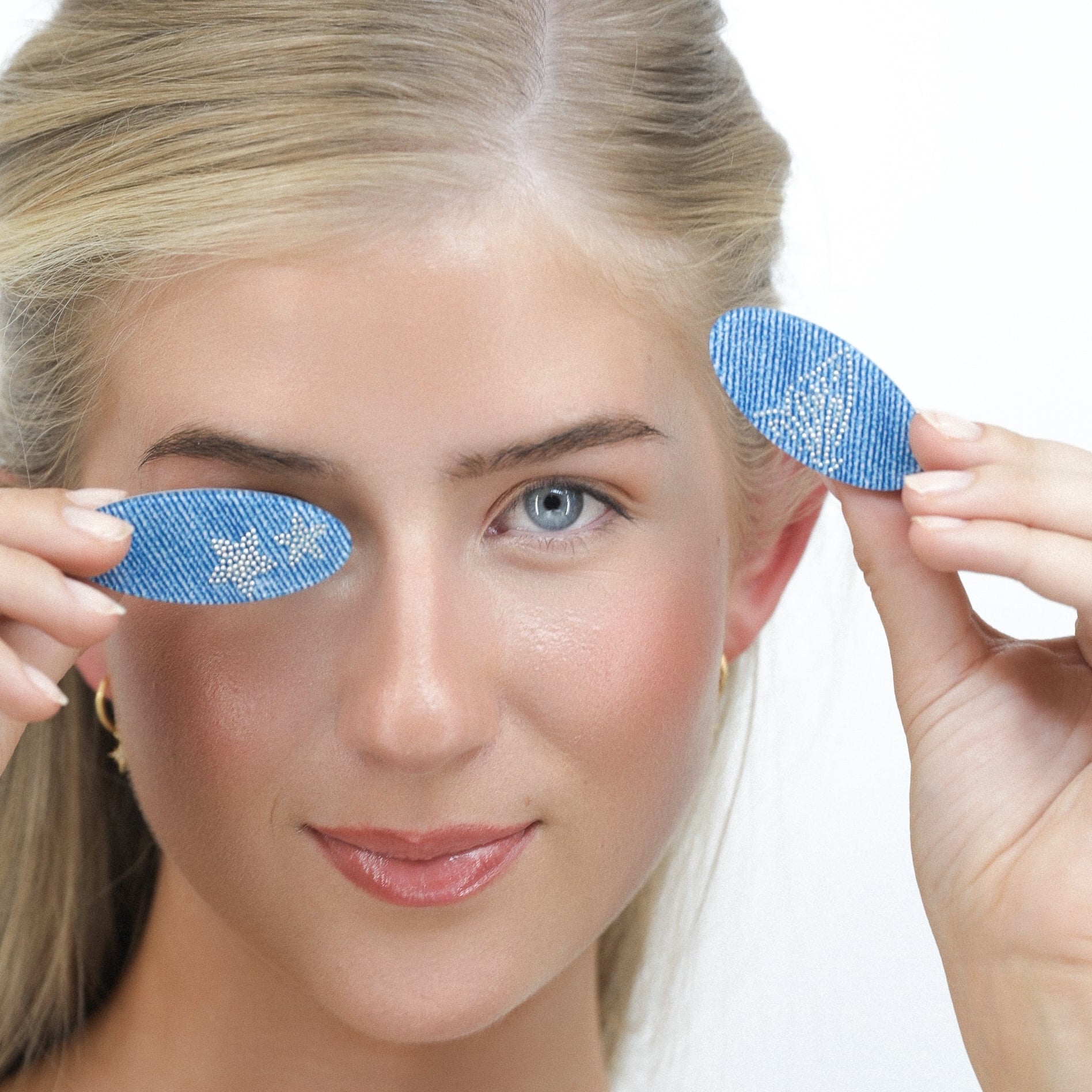 Woman holding Luna Wave blue denim flatter hair clips above her eyes against a white background