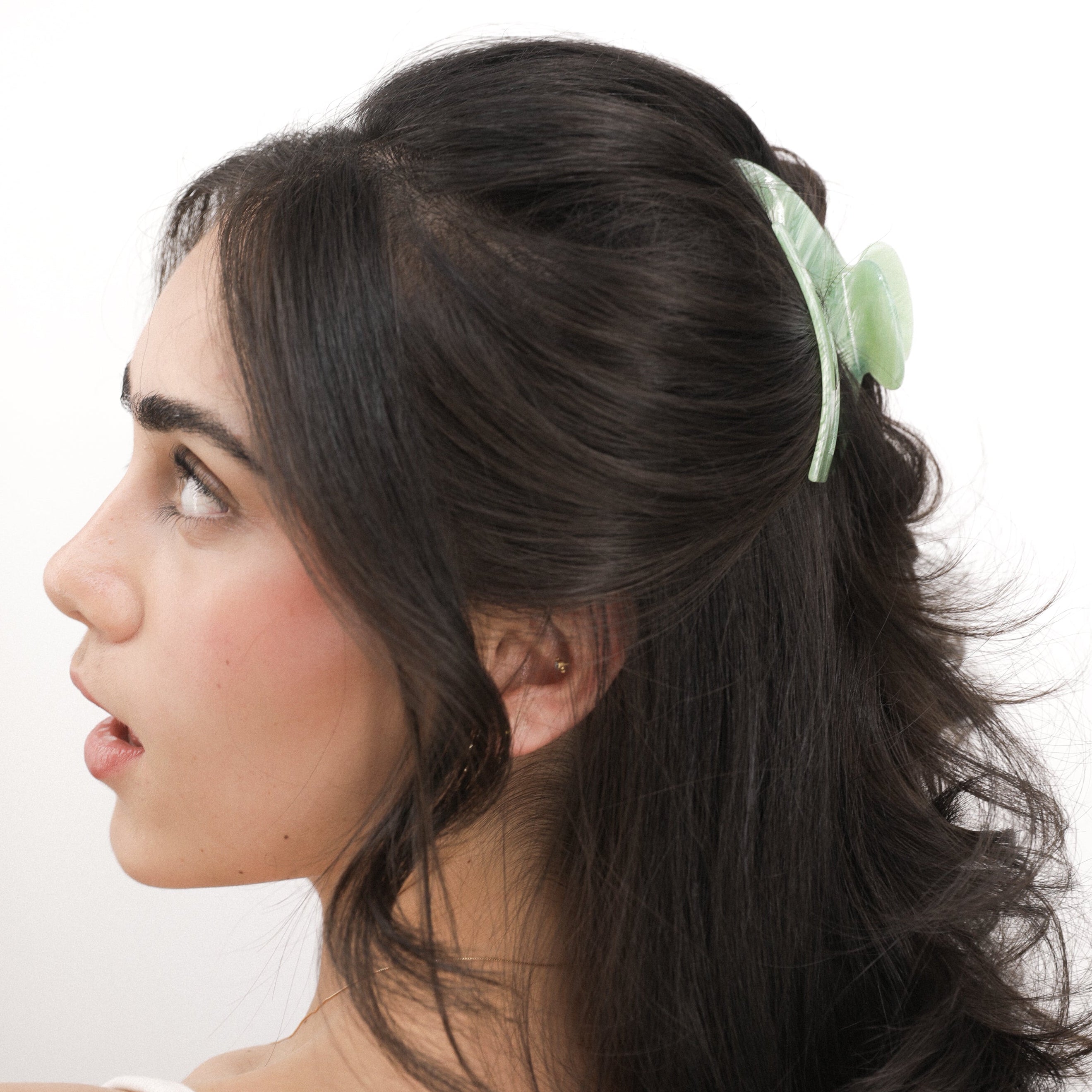 Woman with long dark hair styled in an elegant updo with a Luna Wave green jade earth hair claw clip on a white background