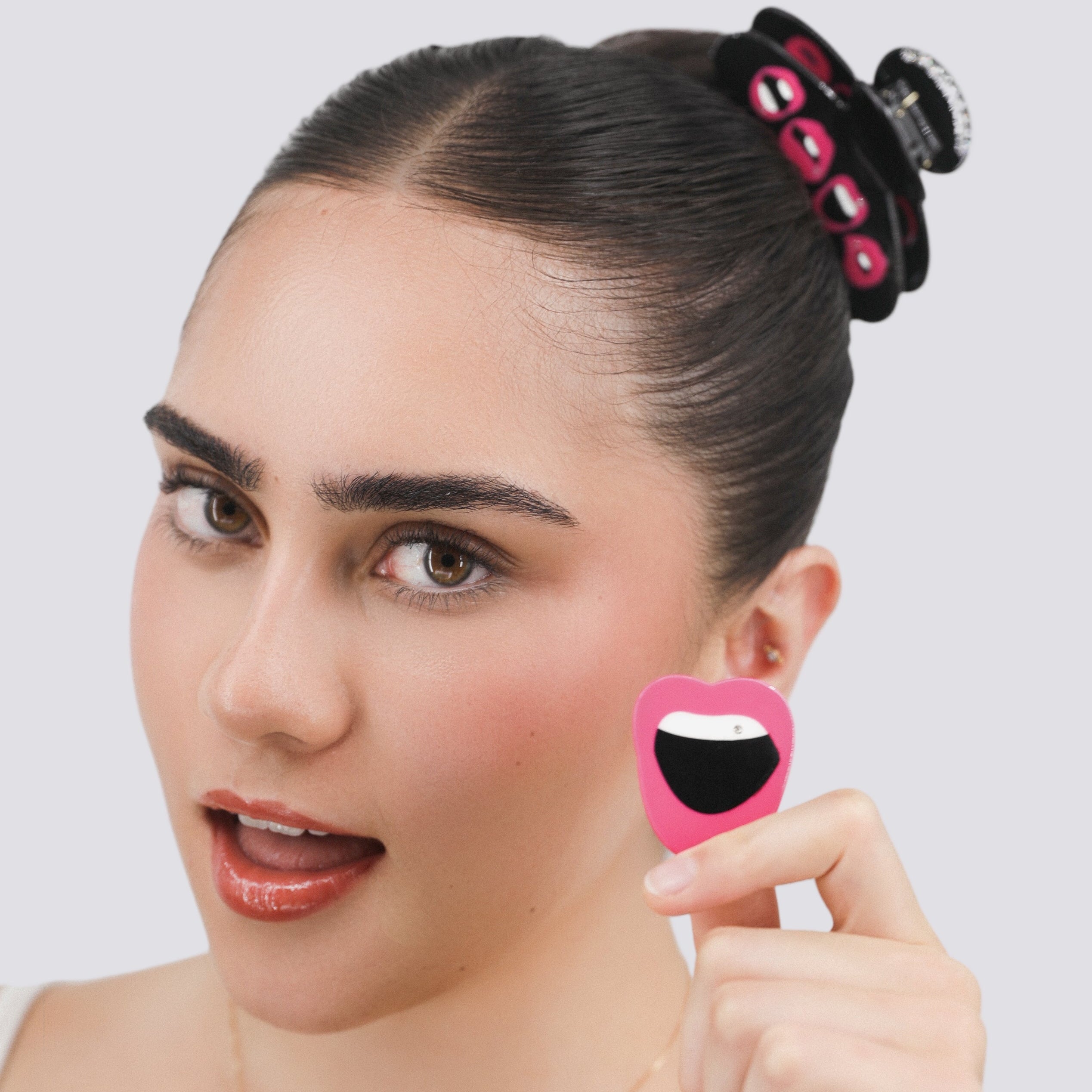 Woman holding a Luna Wave pink lip hair clip with a smiley face on it against a white background