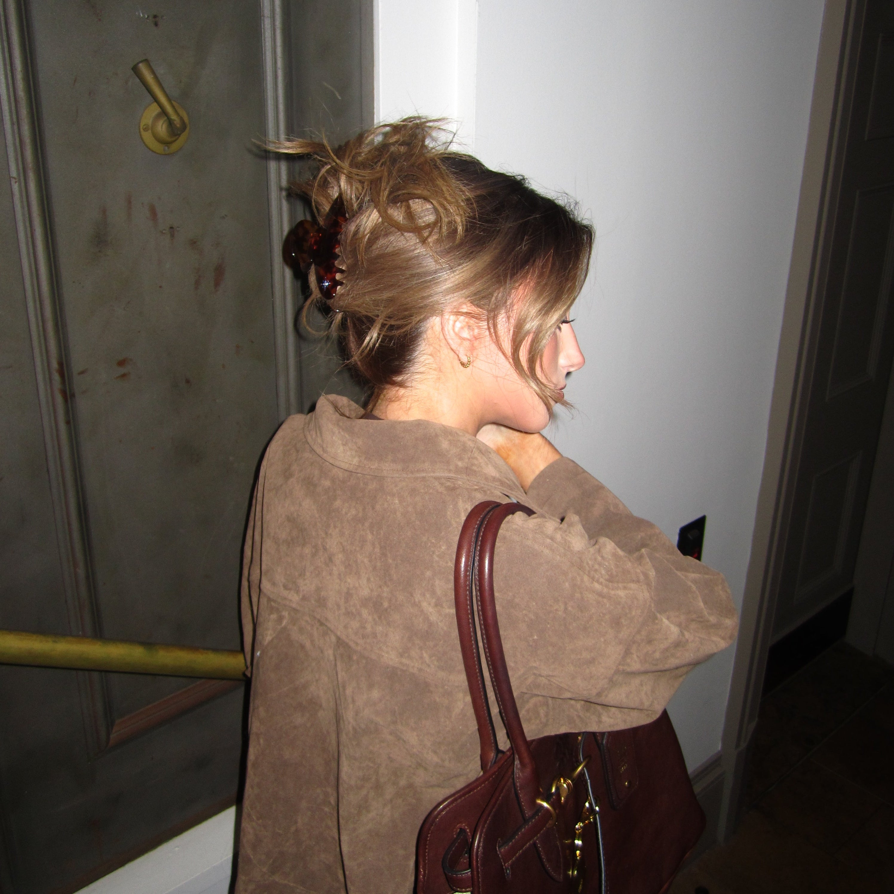 Person wearing a brown coat leaning against a door with a Luna Wave amber starlet large claw clip on the floor.