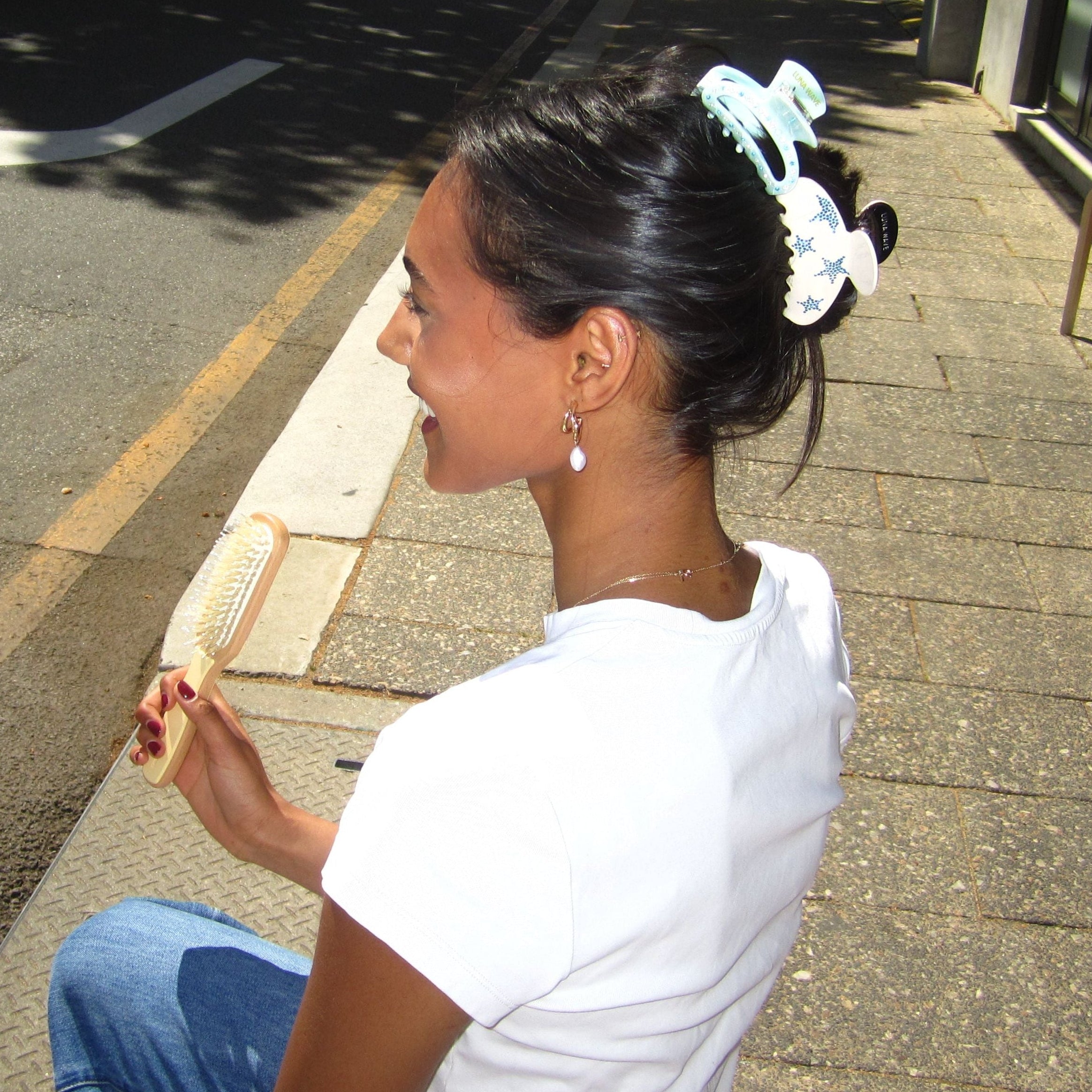 Model sitting on the road wearing Luna Wave blue star claw clip and ice cloud claw