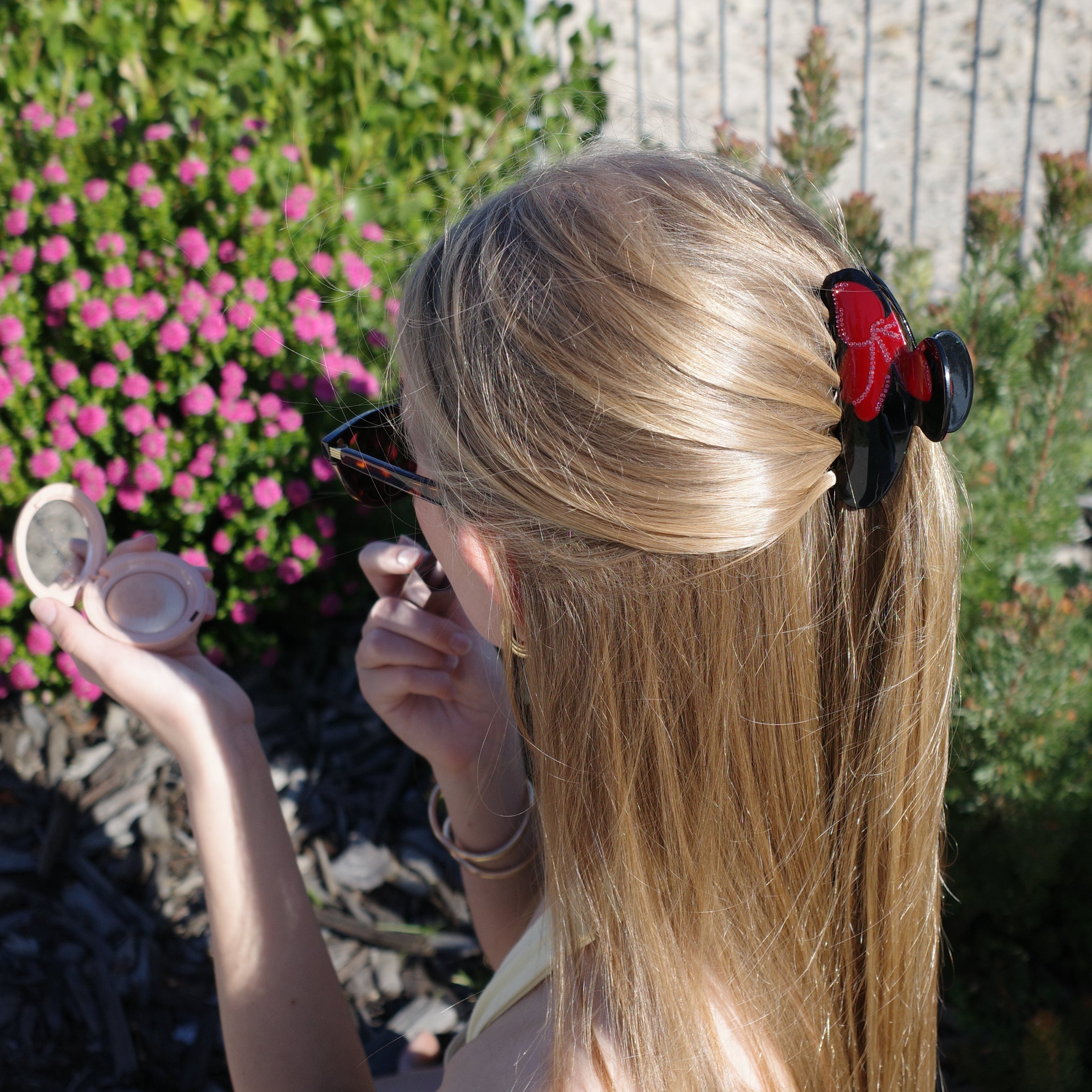 Model with a Luna Wave burgundy blossom claw in front of  pink flowers 