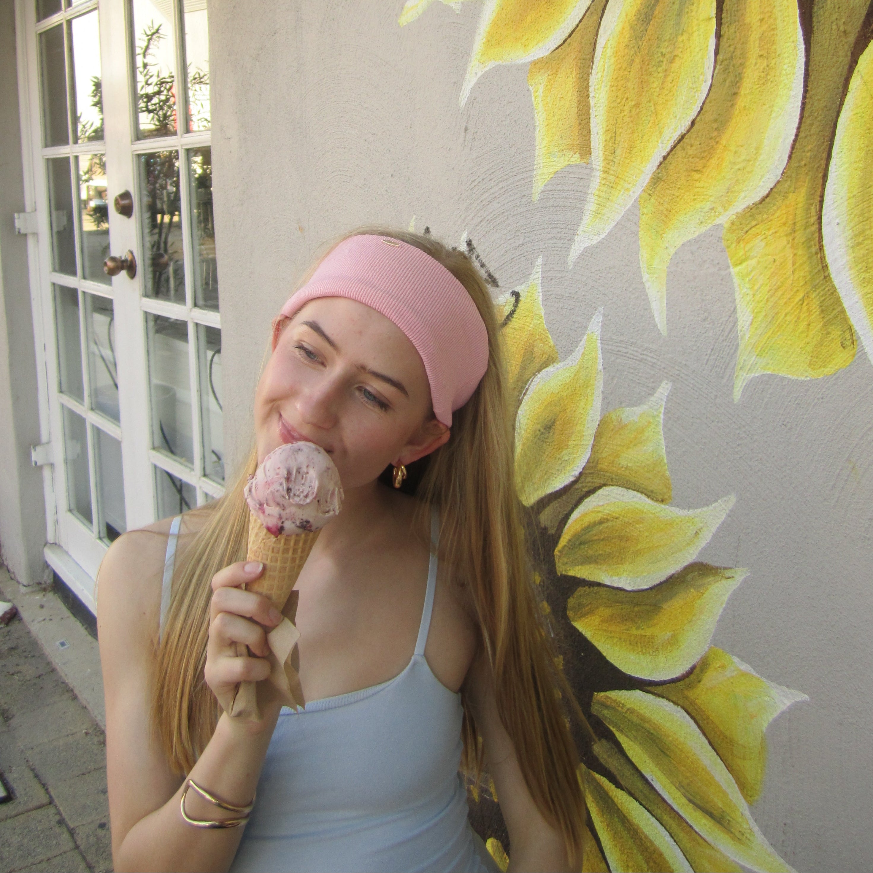 Woman with pink coral soft headband eating ice cream in front of a sunflower mural.