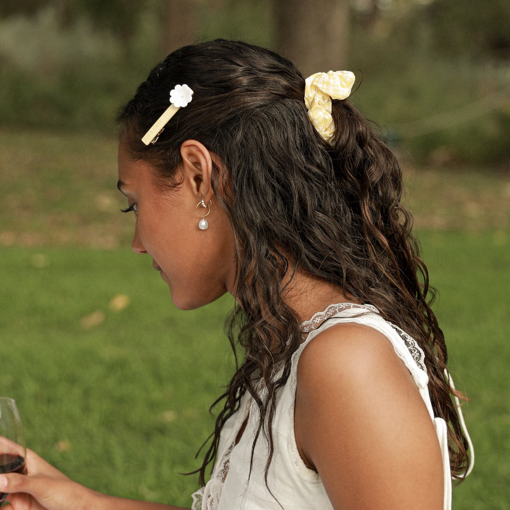 Woman in a white dress with braided hair holding a glass outdoors