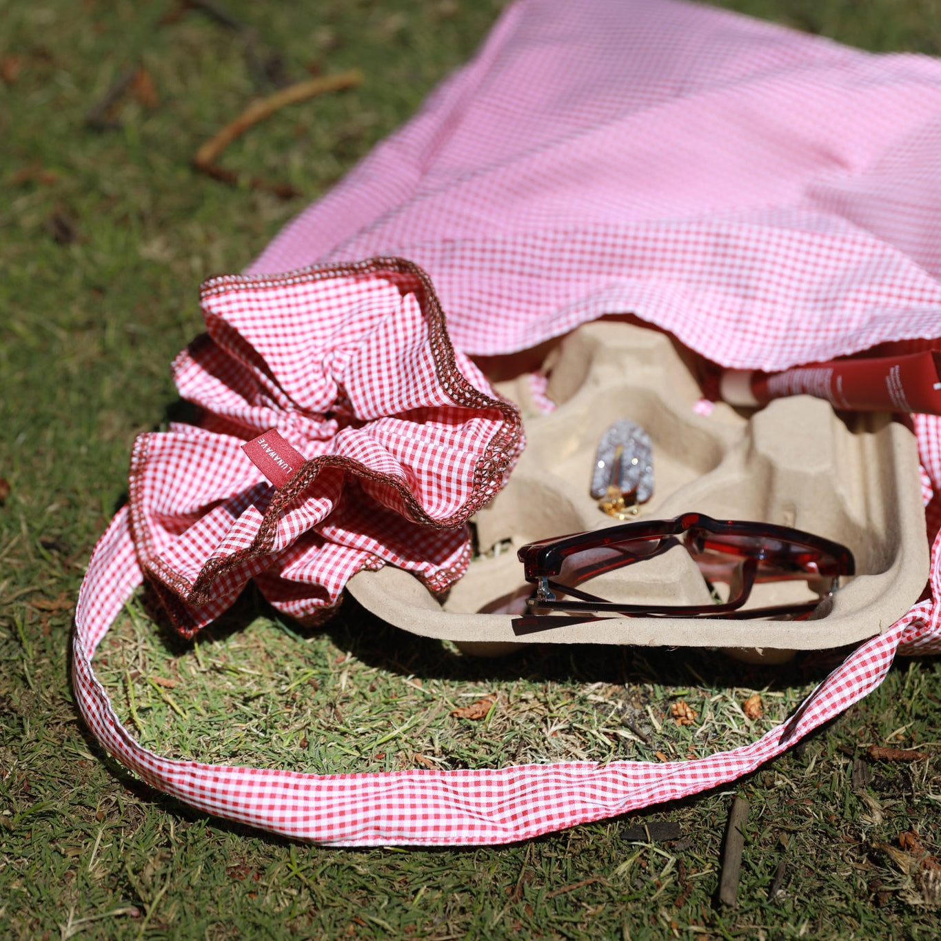 Pink gingham headband with large bow and sunglasses on a grassy background
