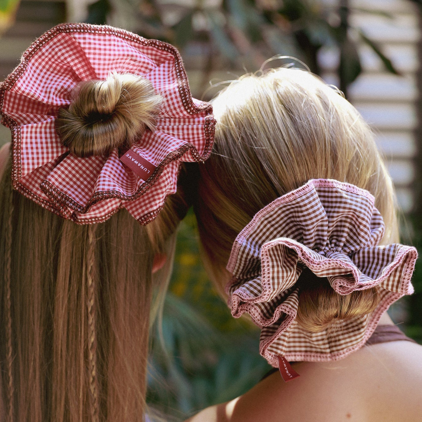 Two women with checkered hair scrunchies on their heads, outdoors.