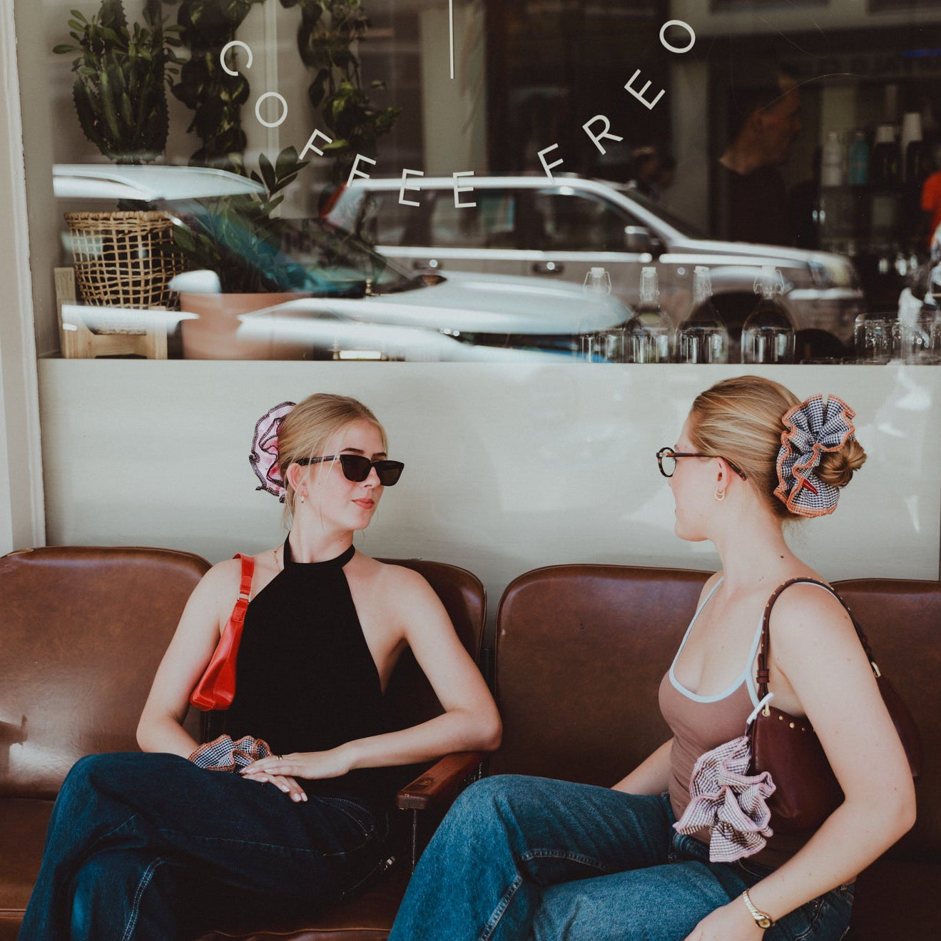 Two women sitting on a brown couch in a coffee shop with luna wave scrunchie.