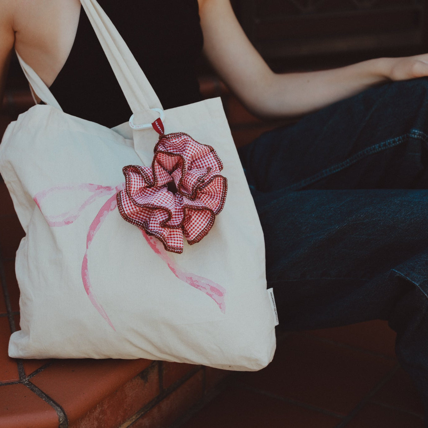 Person holding a white tote bag with a pink flower design on a tiled floor.