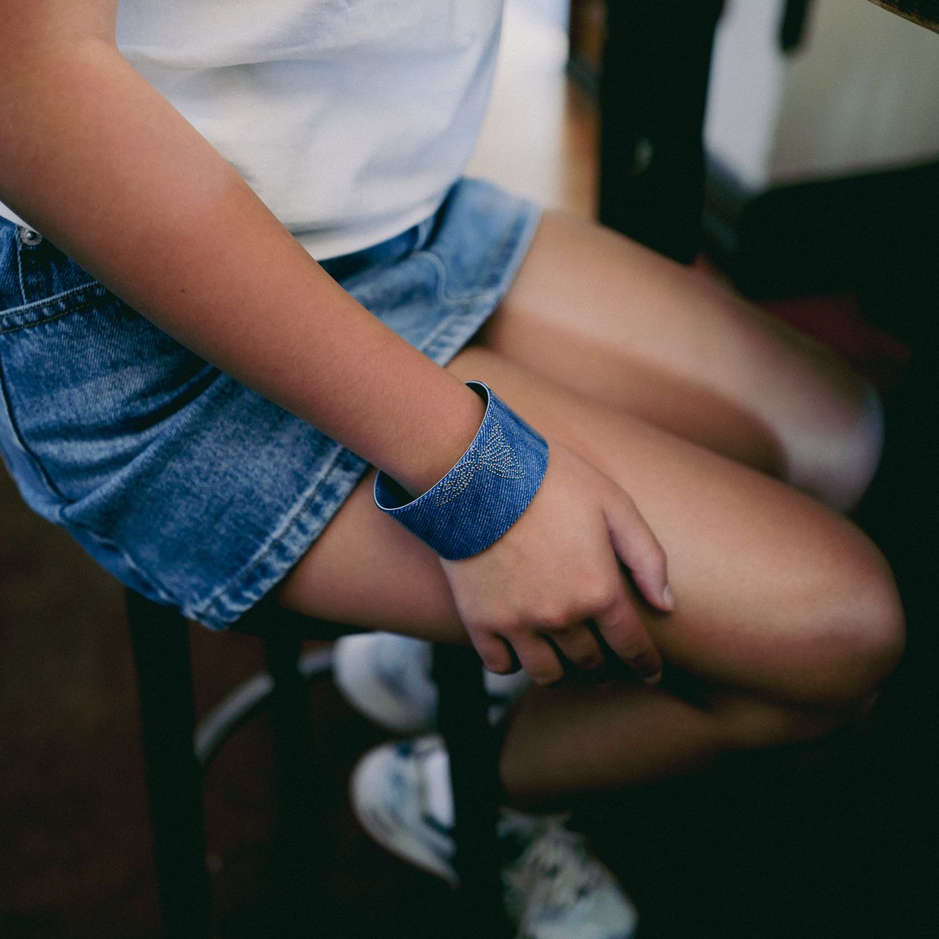 Person wearing a luna wave blue denim flatter bracelet sitting on a chair.