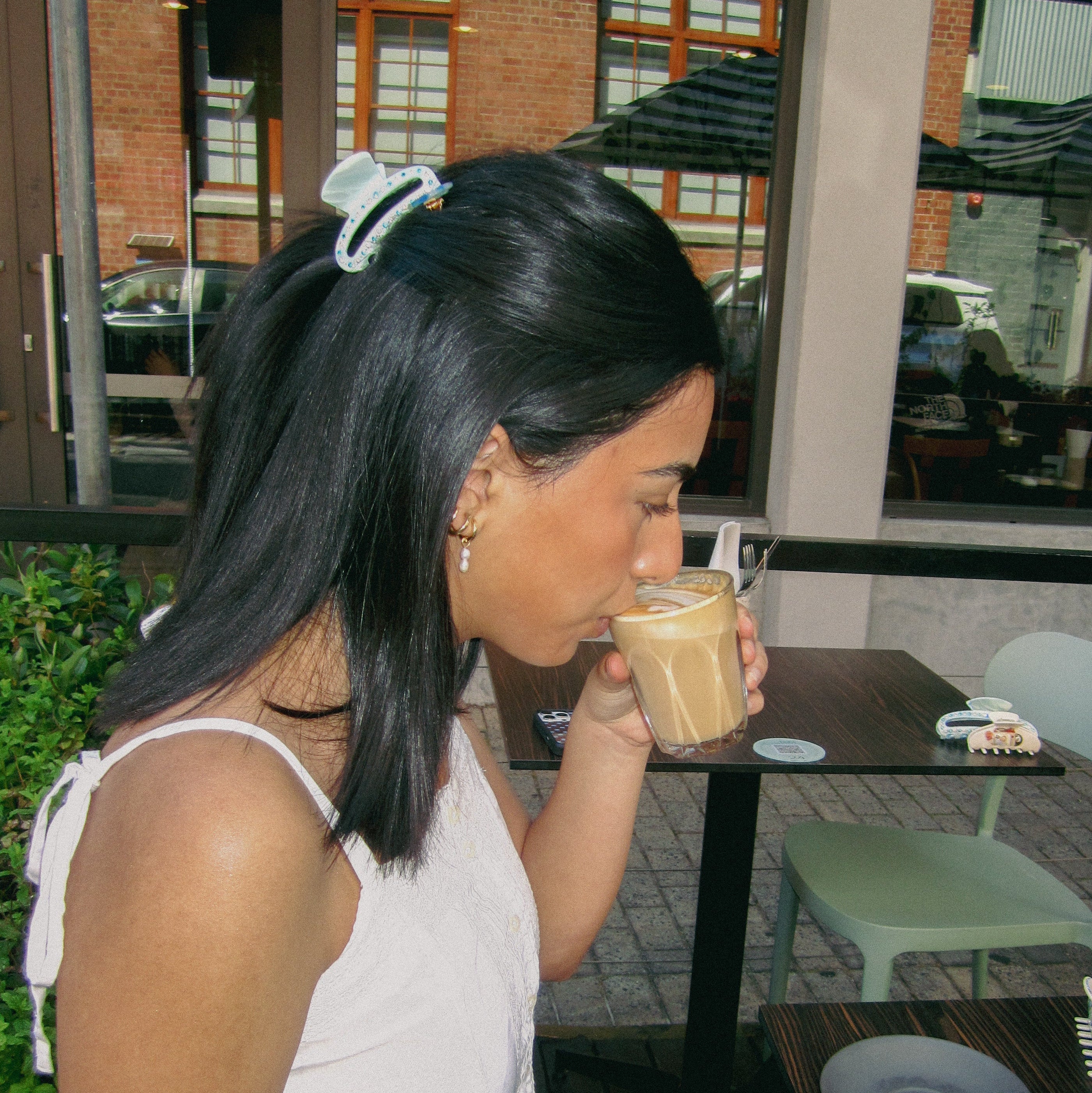 Luna Wave model drinking coffee with ice cloud midi claw at an outdoor cafe.