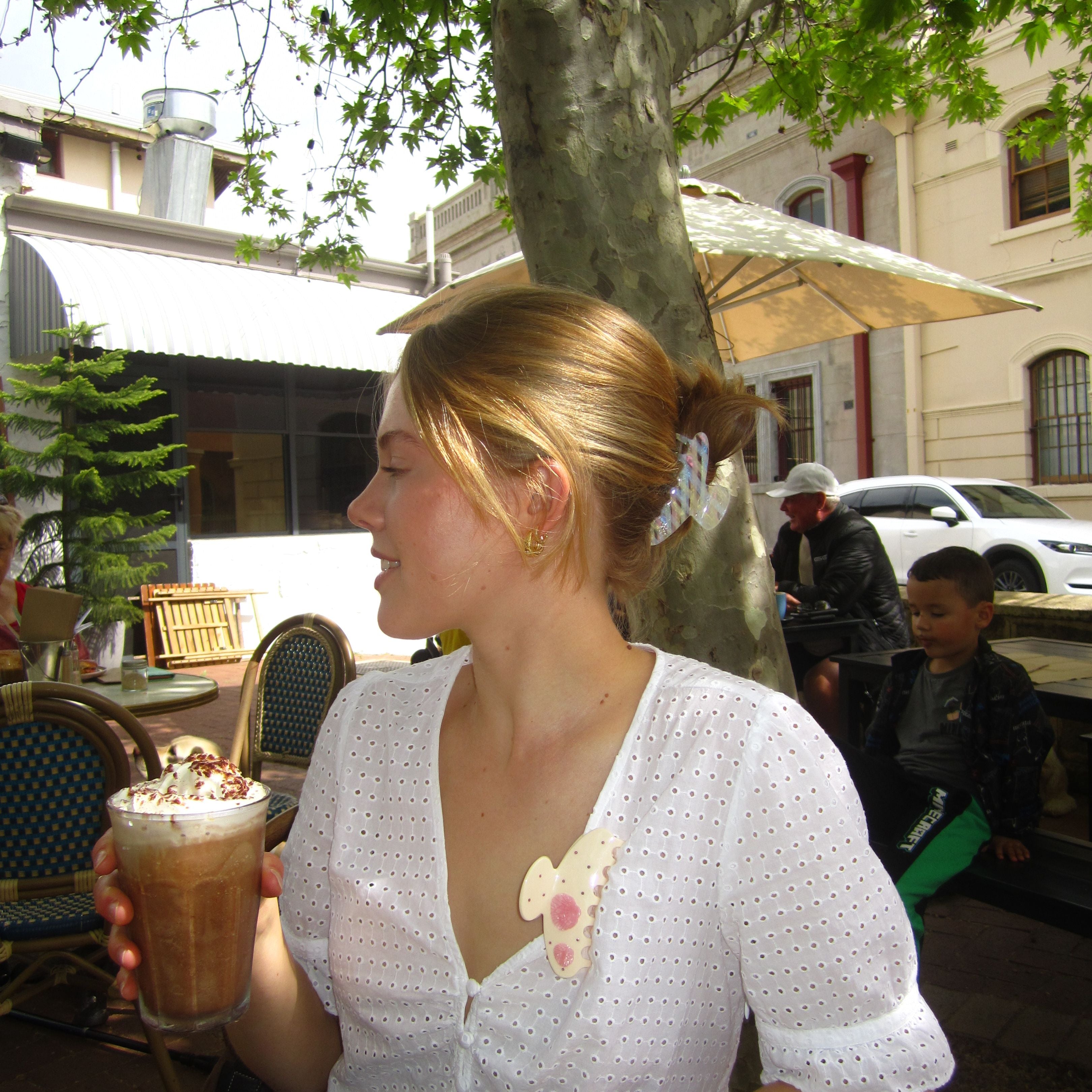 Model holding a drink outdoors with a tree and building in the background wearing Luna Wave initial claw clip K and calista claw