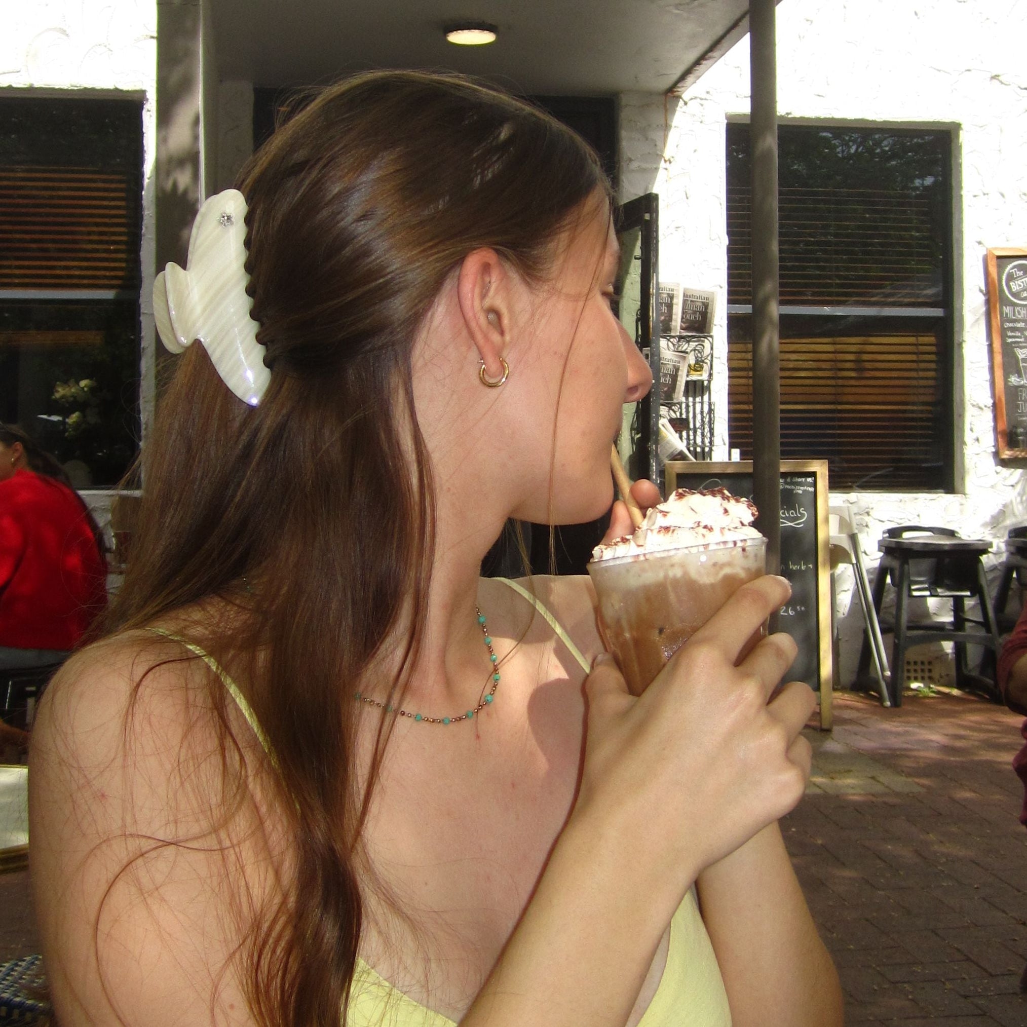 Woman in a yellow top holding a drink in an outdoor cafe setting wearing ivory pearl claw 