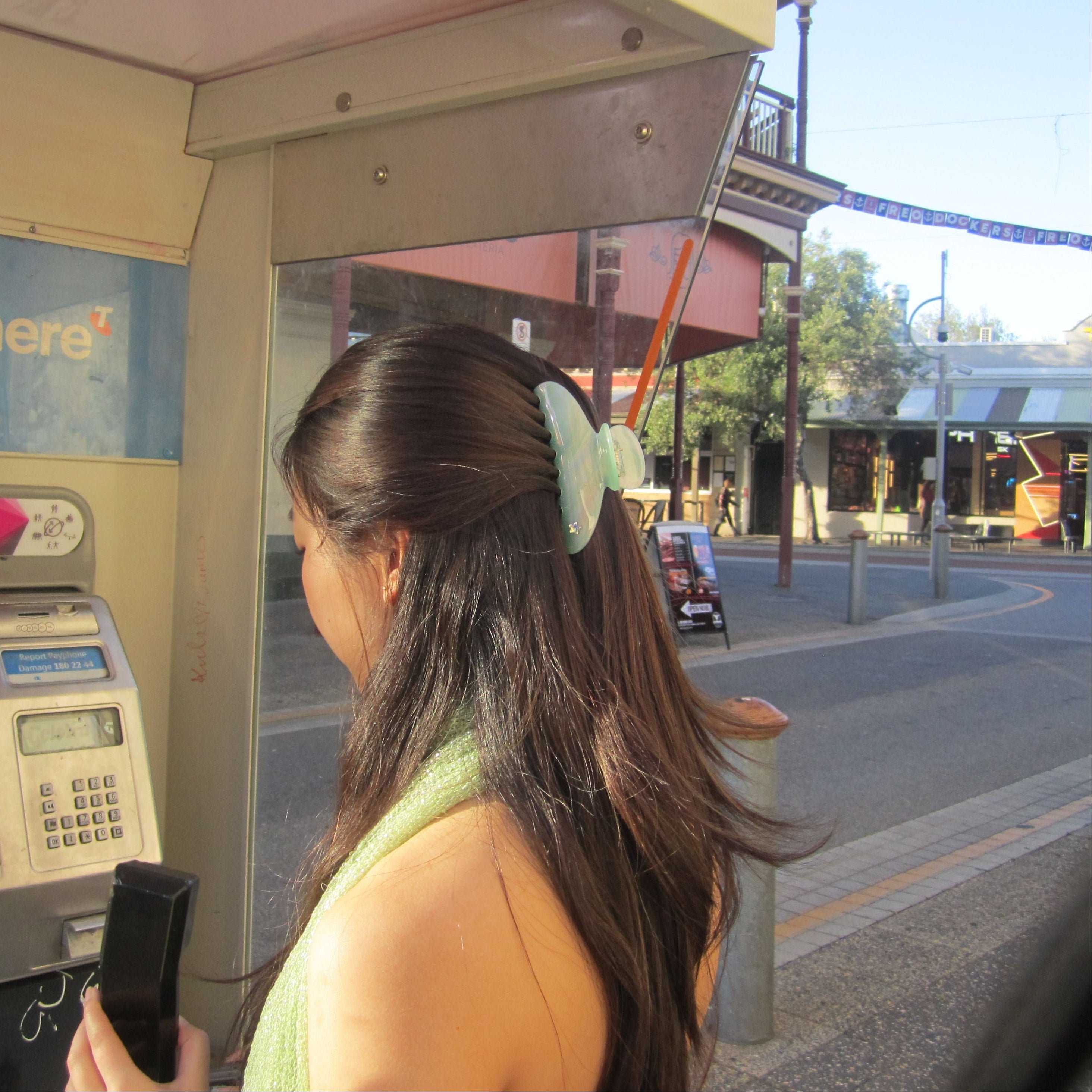 Woman using  a public phone on a street wearing Luna Wave jade pearl claw