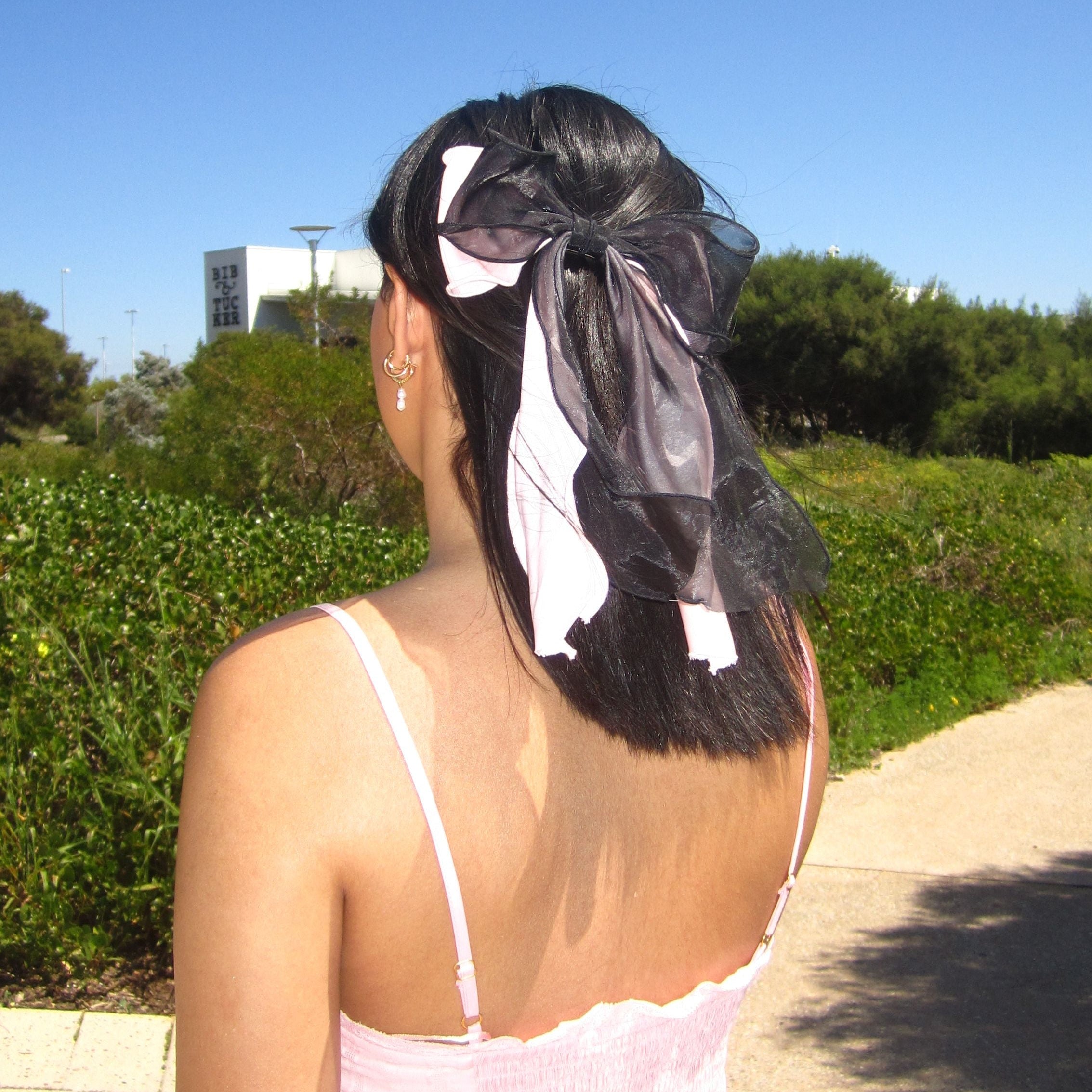 A young lady with a Luna Wave lacy barrette in her hair walking on a path with greenery and blue sky.