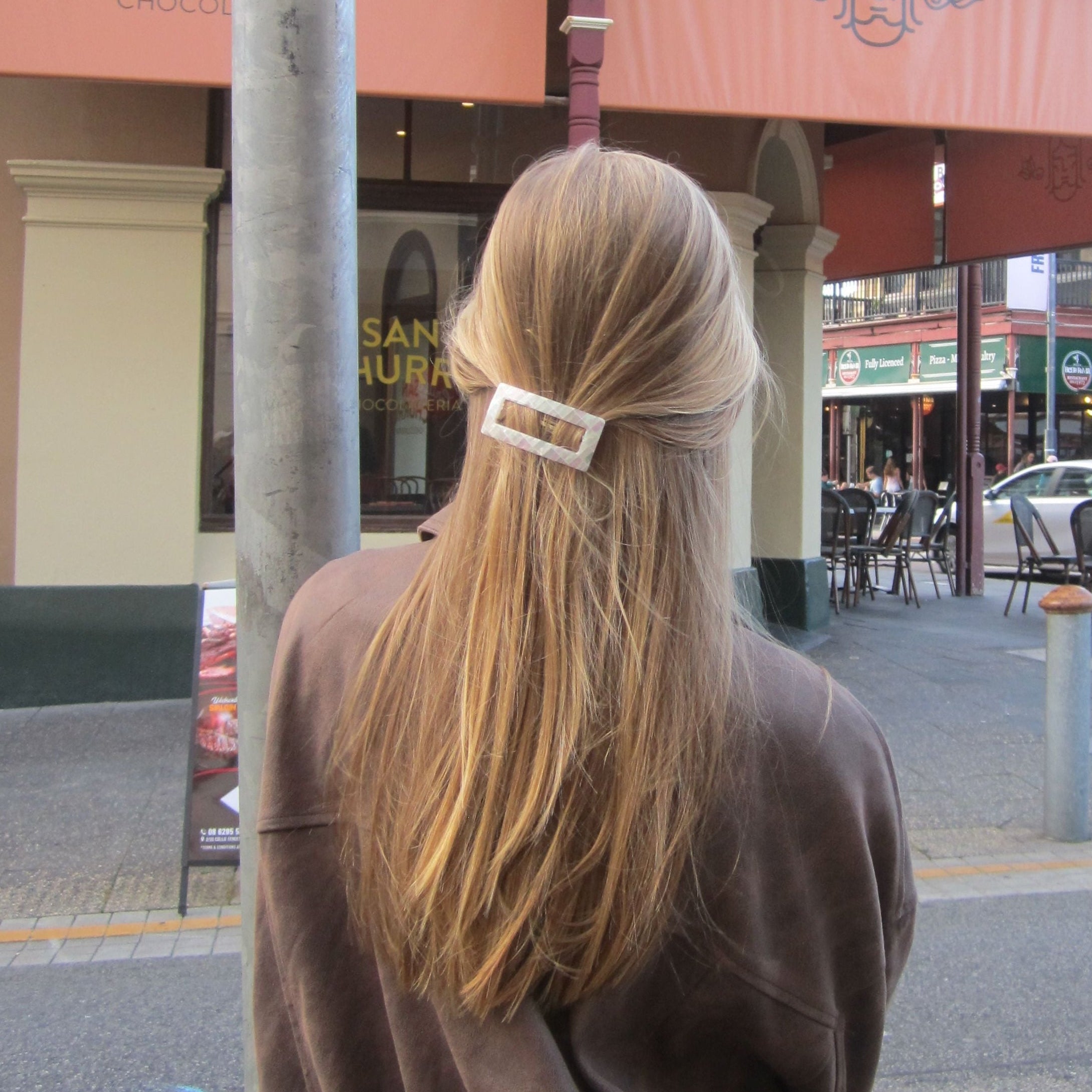 Person with long hair wearing opal earth barrette standing on a street with shops in the background