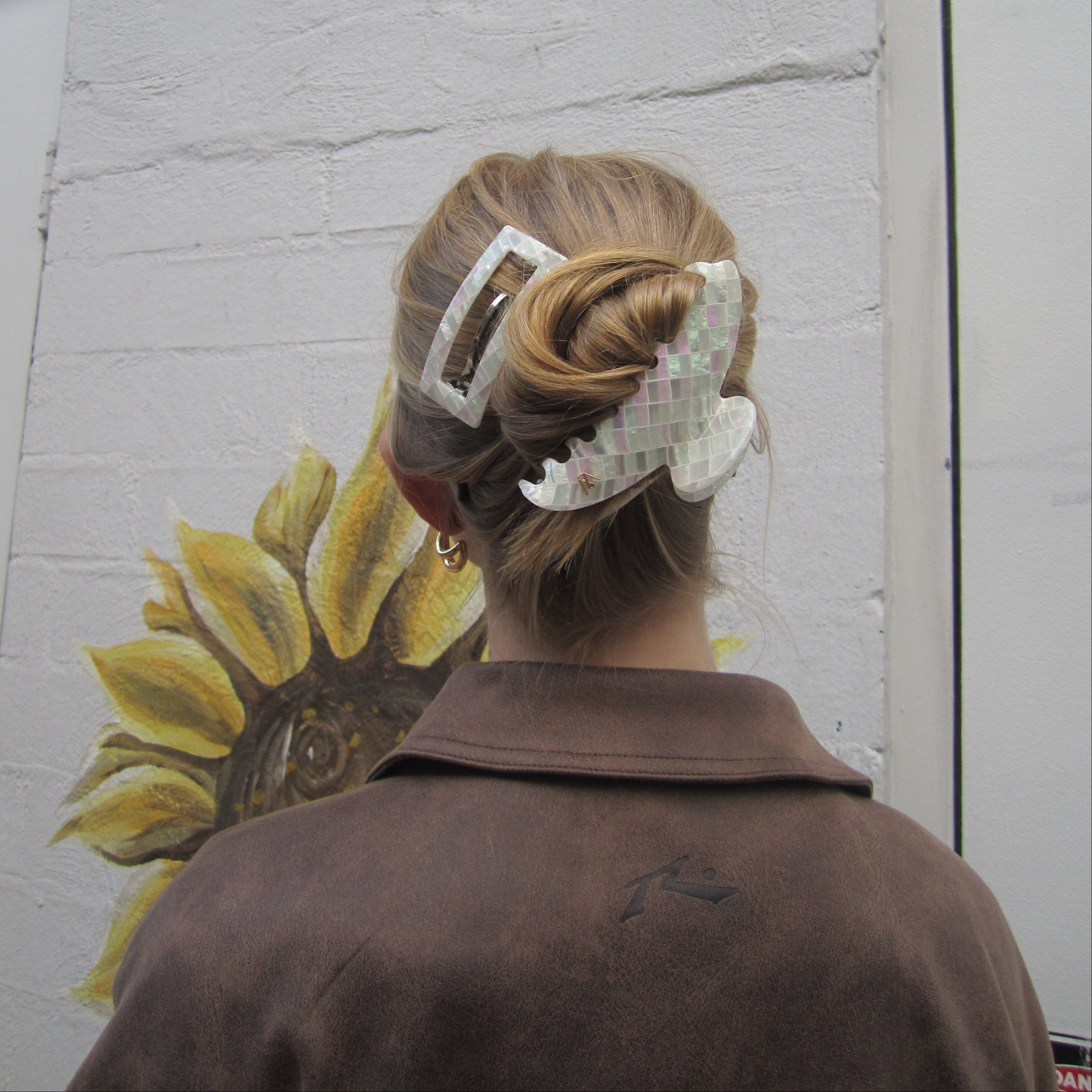 Person with a Luna Wave opal earth claw  clip standing next to a sunflower drawing on a wall.