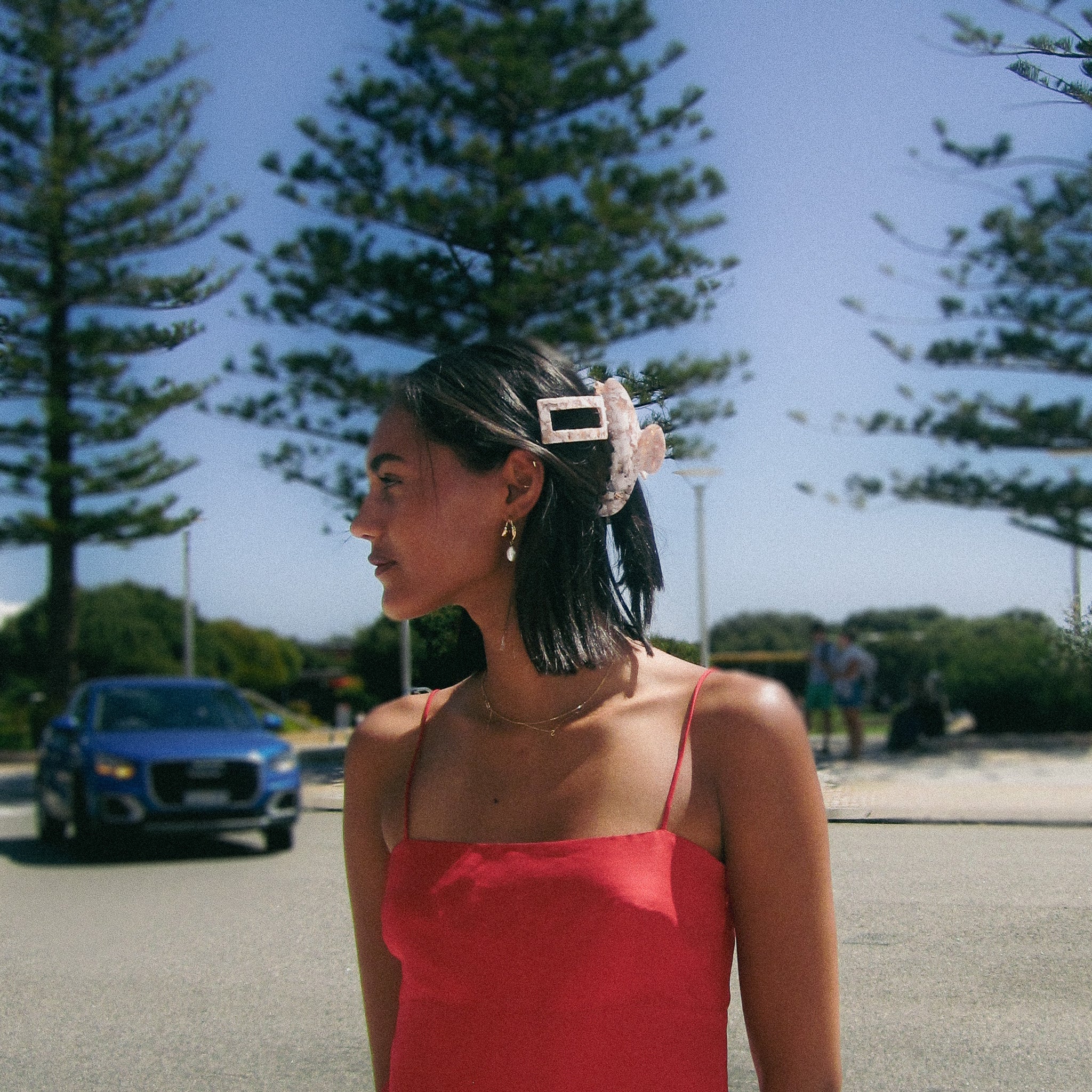 Luna Wave model  in a red dress standing outdoors with pink barrette claw clip