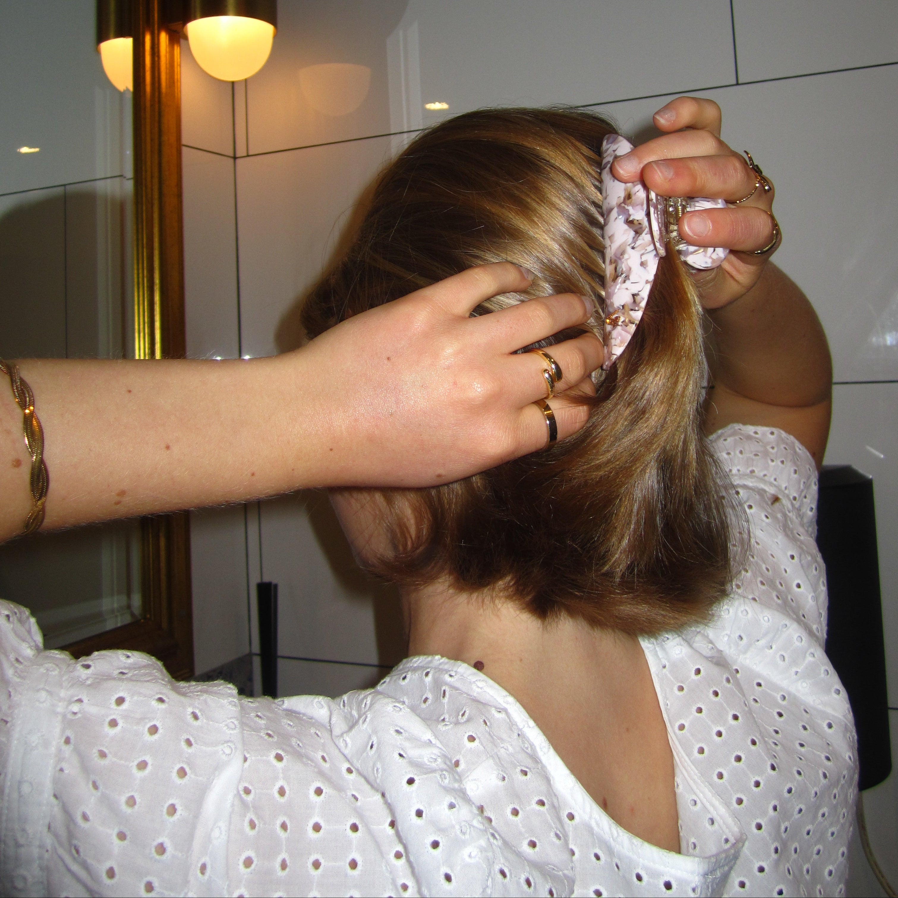 A young lady styling hair with a Luna Wave pink earth claw in a bathroom with a light fixture in the background 