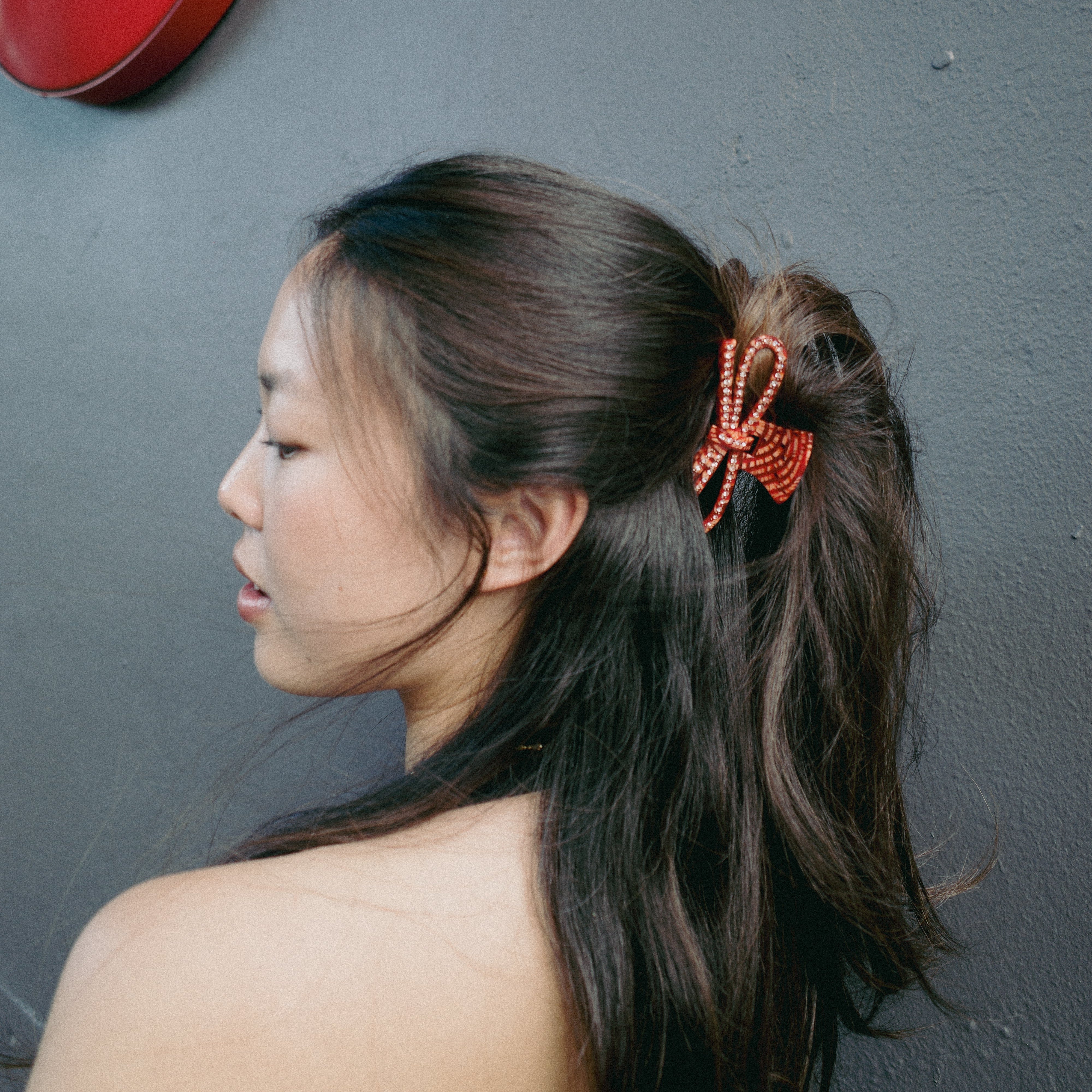 Luna Wave model with a red bow claw clip standing in front of a gray wall