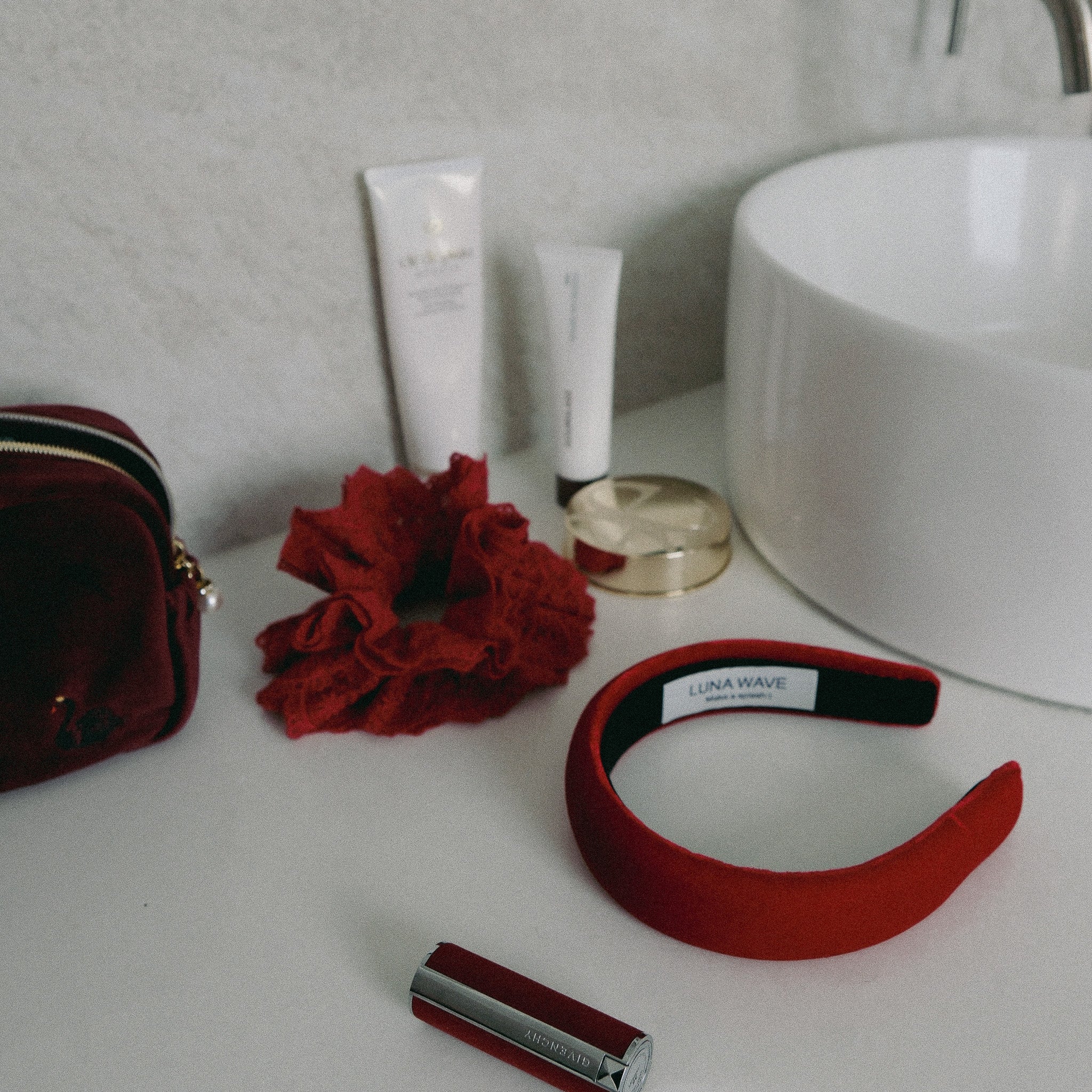 Luna Wave red lace scrunchie, velvet hairband, and pouch on a bathroom counter.