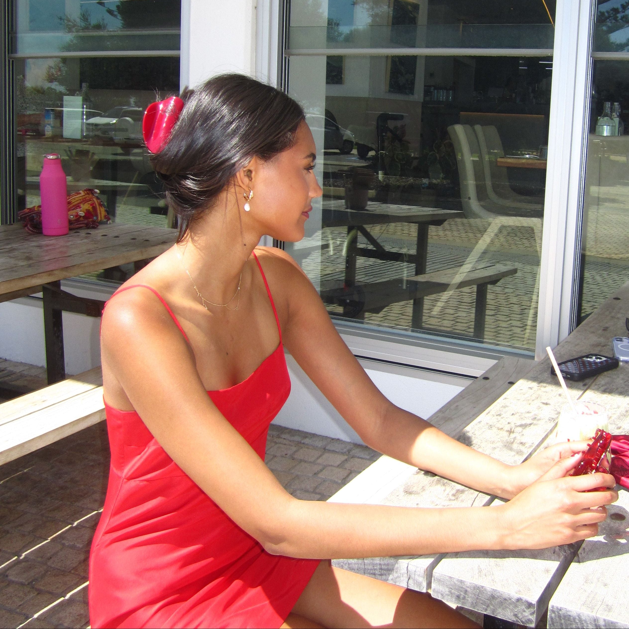 Woman in a red dress holding a red flower in front of a glass door wearing a Luna Wave reverie claw