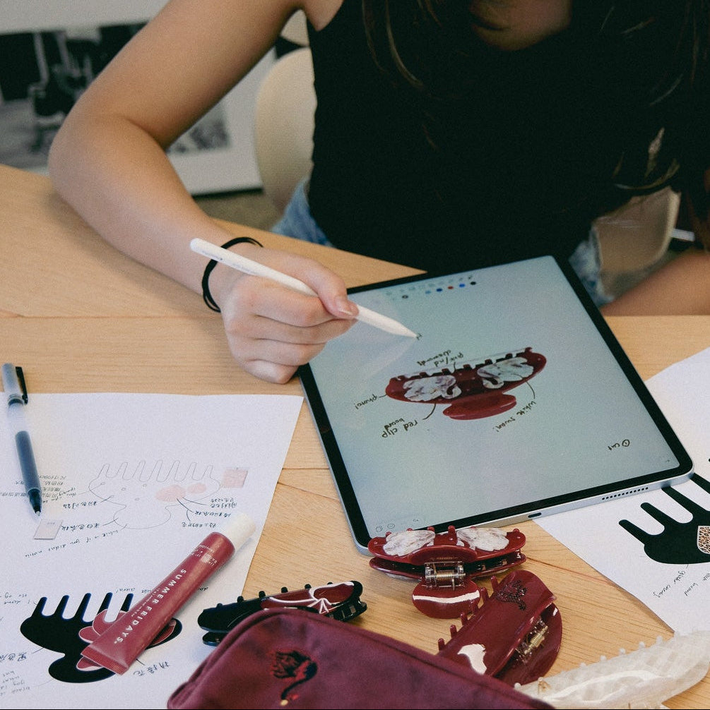 Luna Wave founder Hamie Lyu using a stylus on a tablet with artistic designs for hair accessories