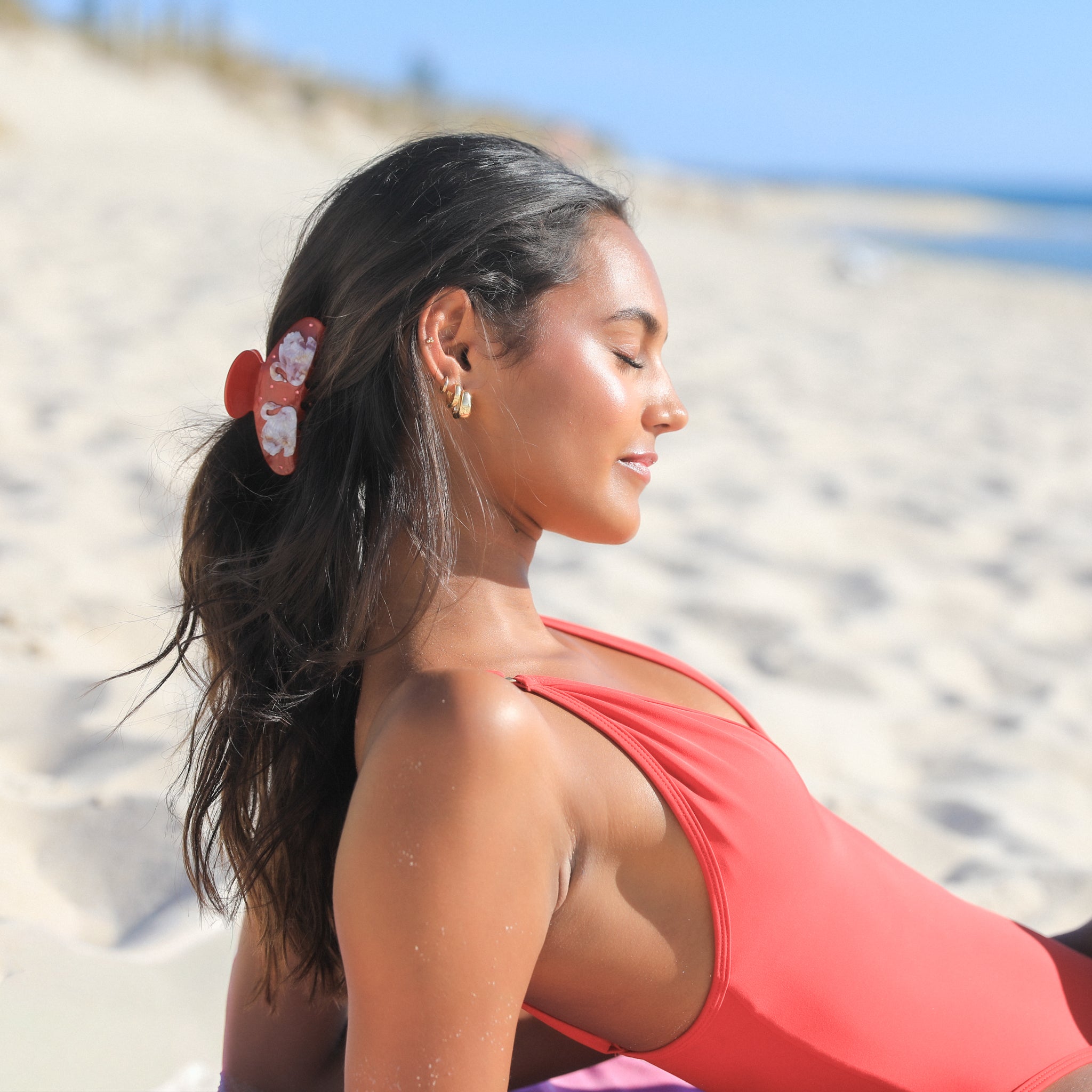 Woman in a red swimsuit with Luna Wave red odette hair claw clip on a sandy beach