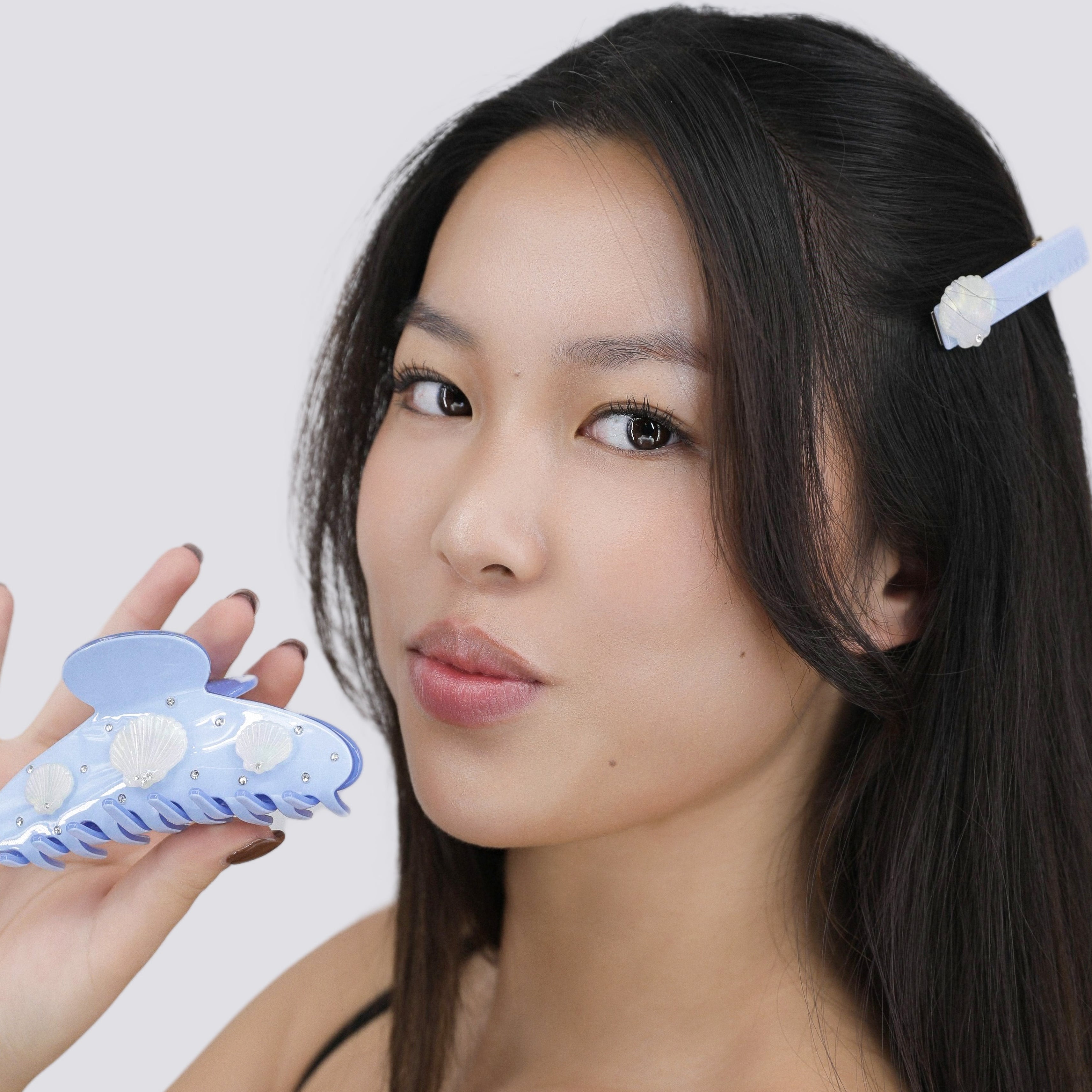 Woman holding a Luna Wave blue marina hair claw clip against a plain background