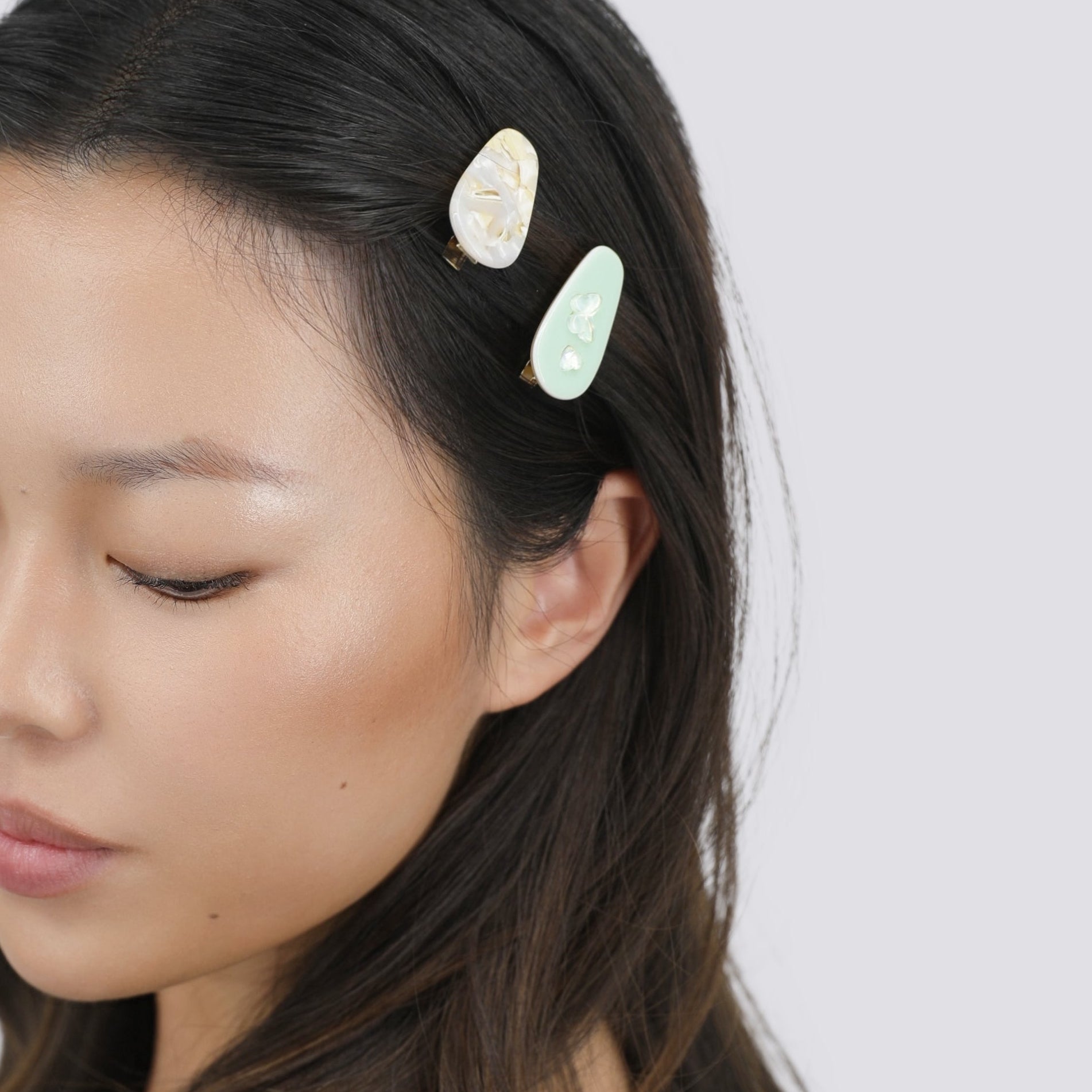 Woman with long dark hair wearing two Luna Wave petite hair clips on a light white background