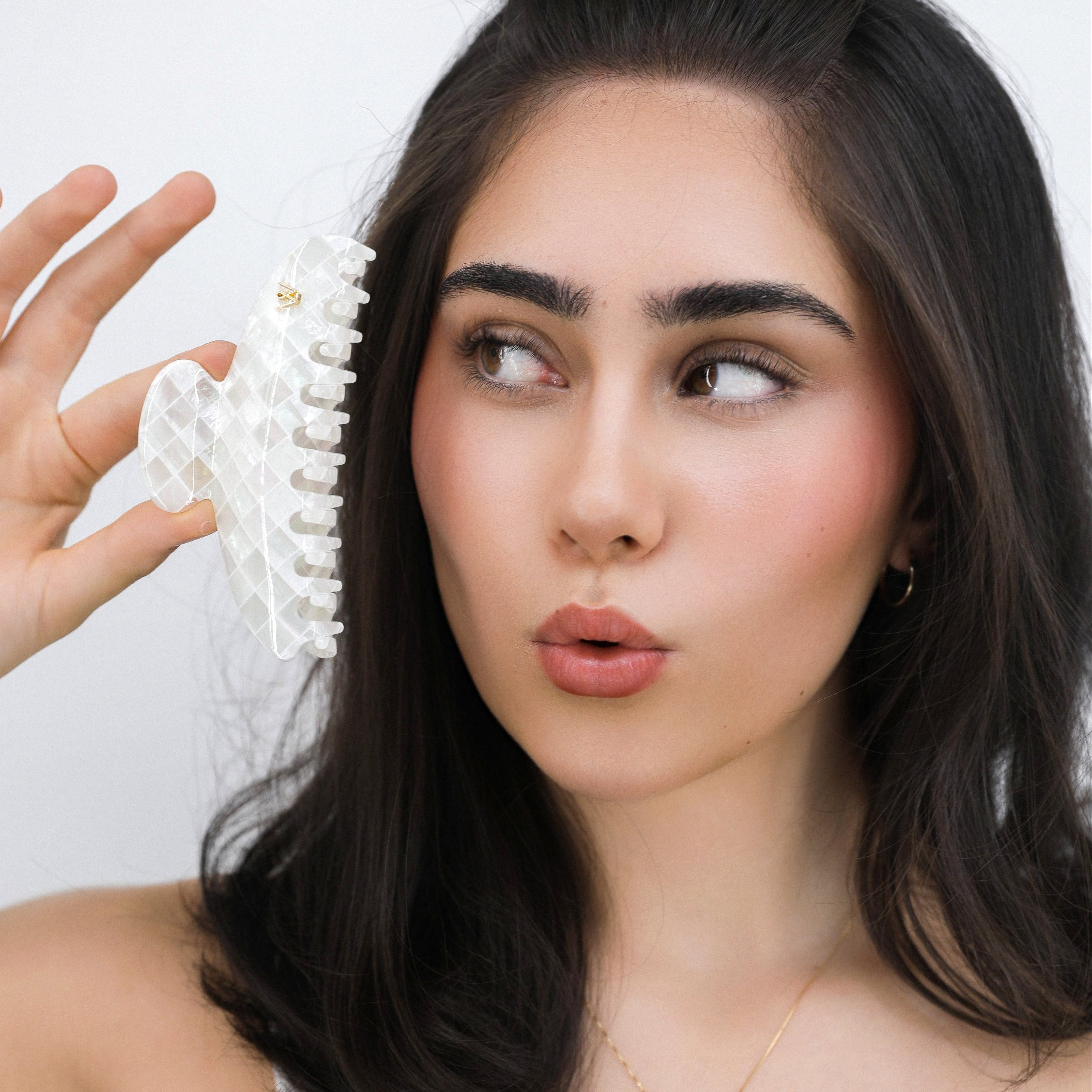 Woman holding a Luna Wave white opal earth hair claw clip near her face against a white background