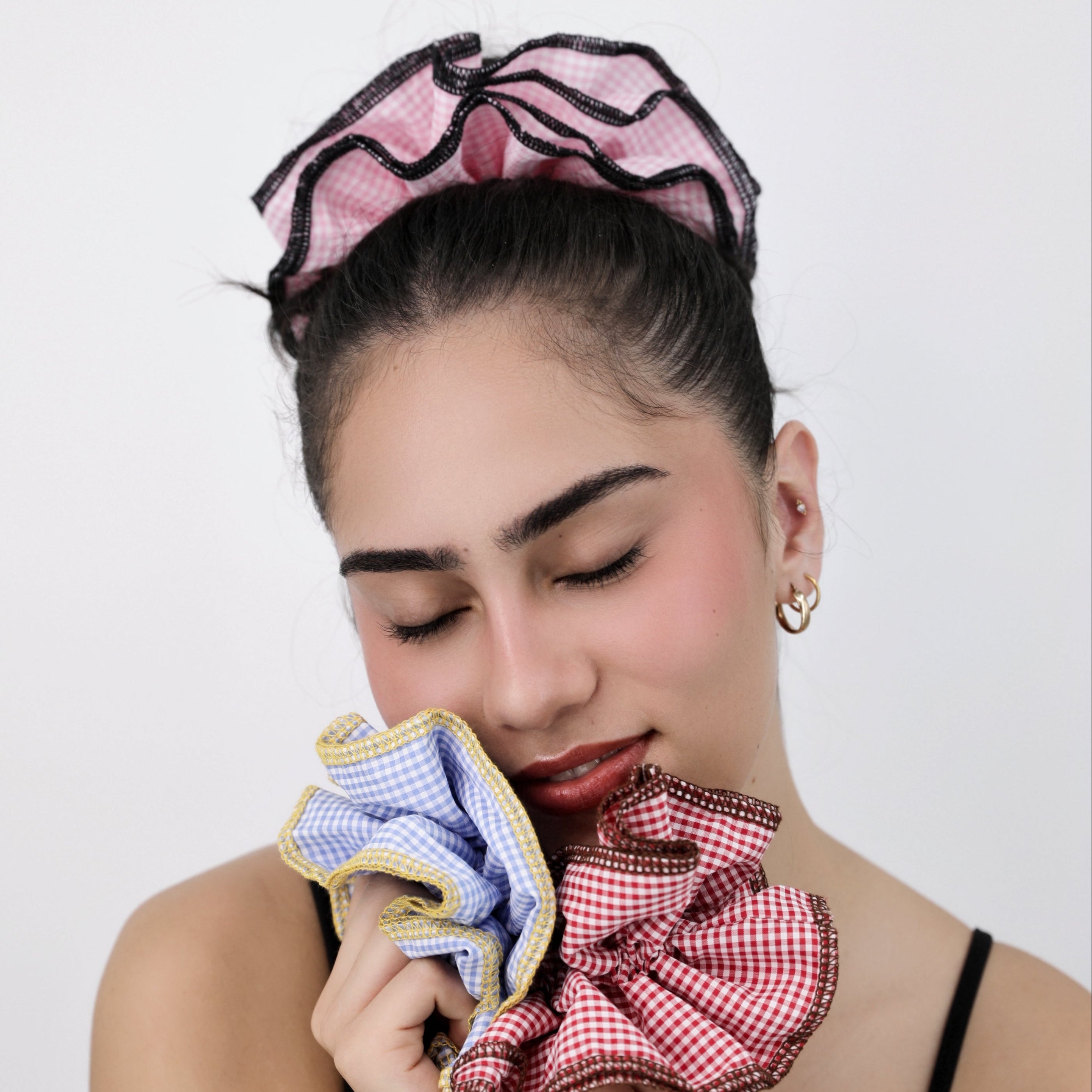 Woman holding colourful hair scrunchie and wearing Luna Wave pink check scrunchie against a white background