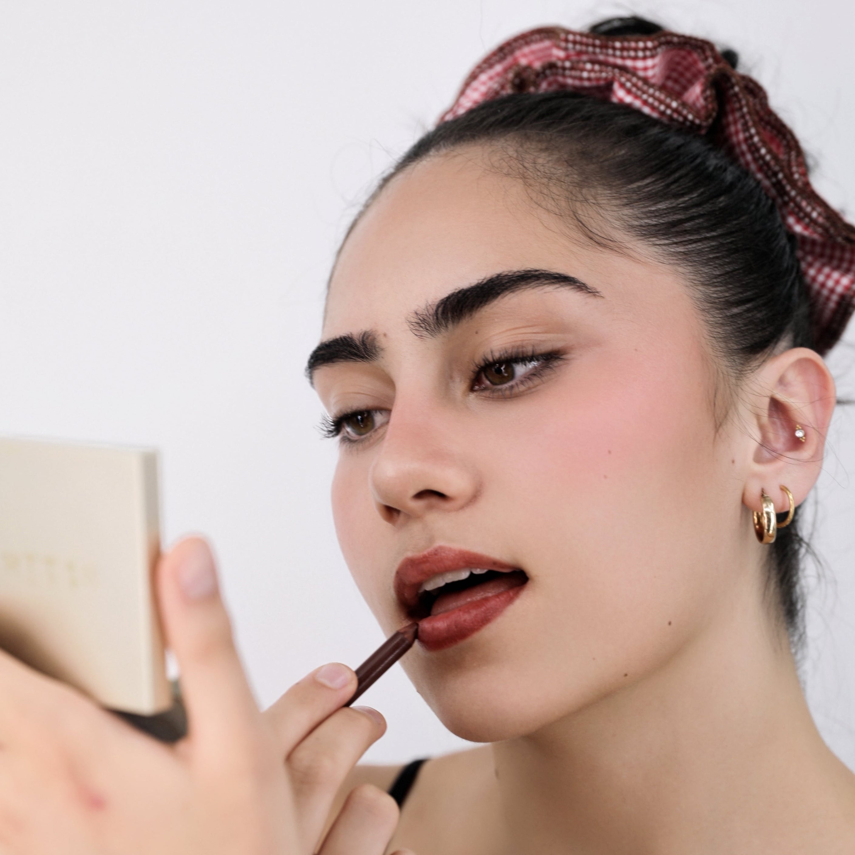 Woman applying lipstick in front of a mirror with Luna Wave red darling duo scrunchie