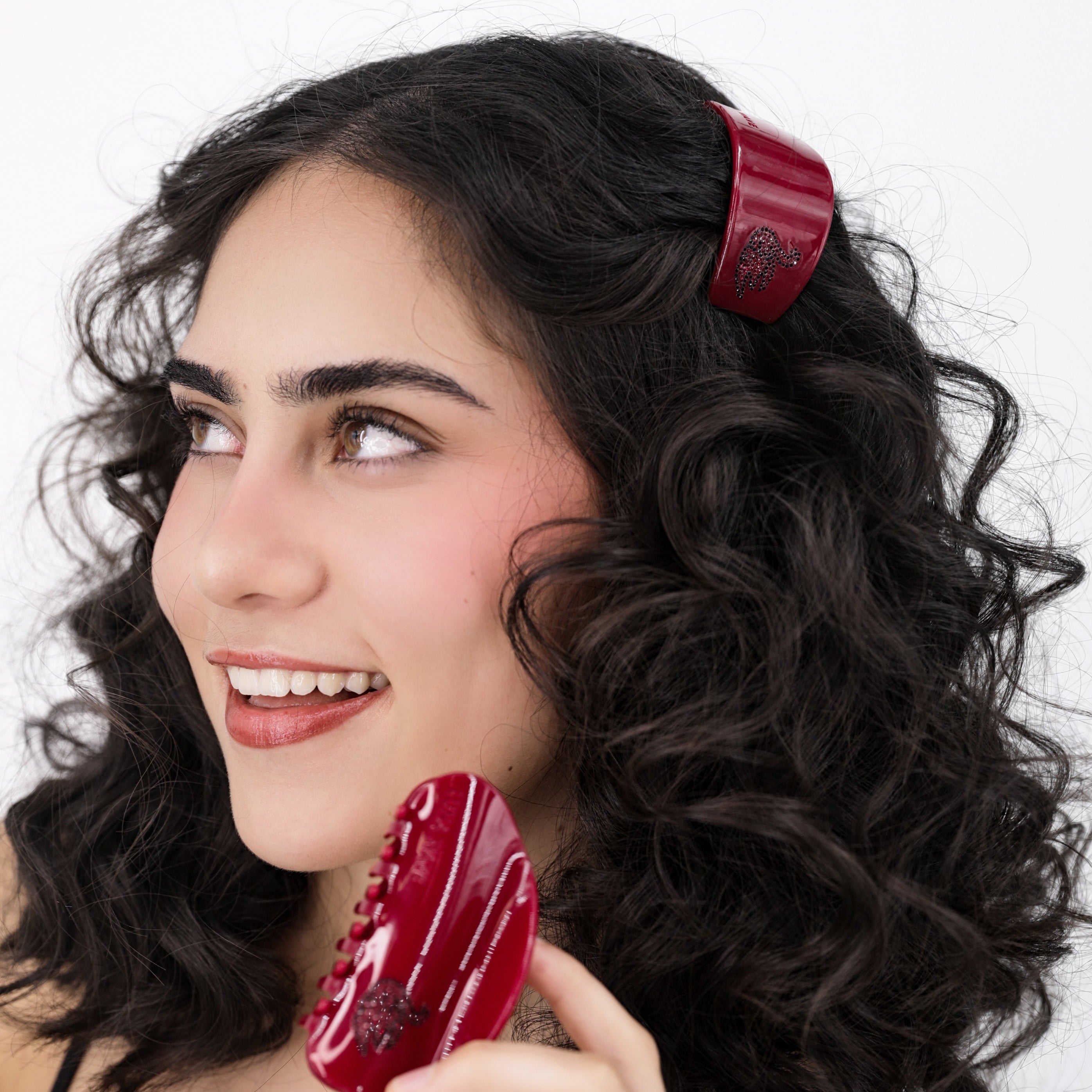 Woman with curly hair wearing a Luna Wave red odette hair barrette against a white background
