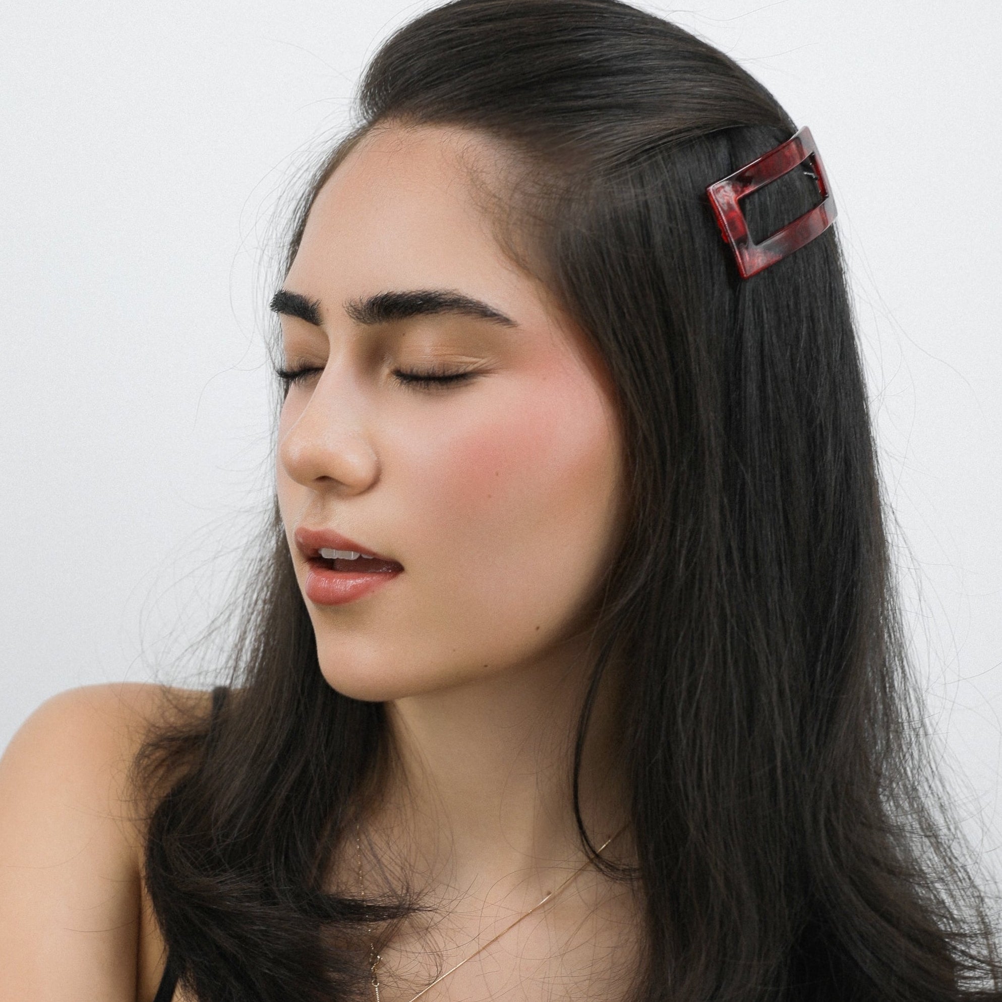 Woman with long black hair getting her hair sprayed with a Luna Wave red ruby earth hair barrette against a white background