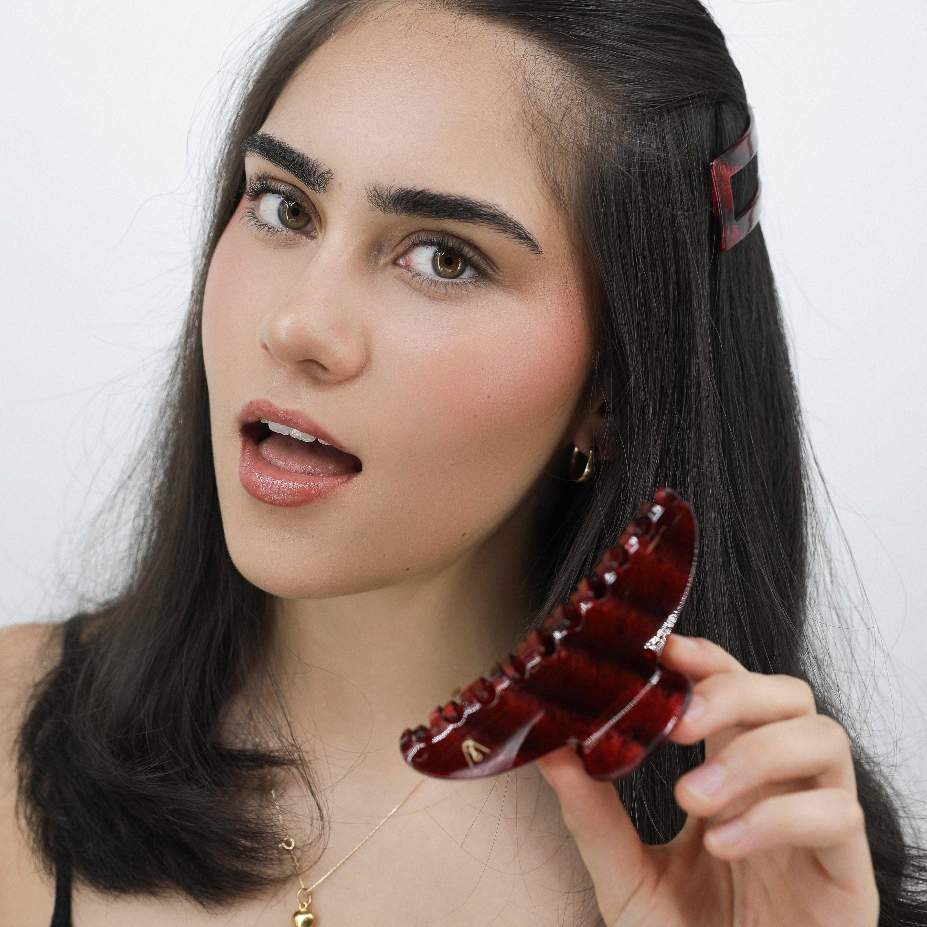 Woman holding a Luna Wave red ruby earth hair claw clip against a white background