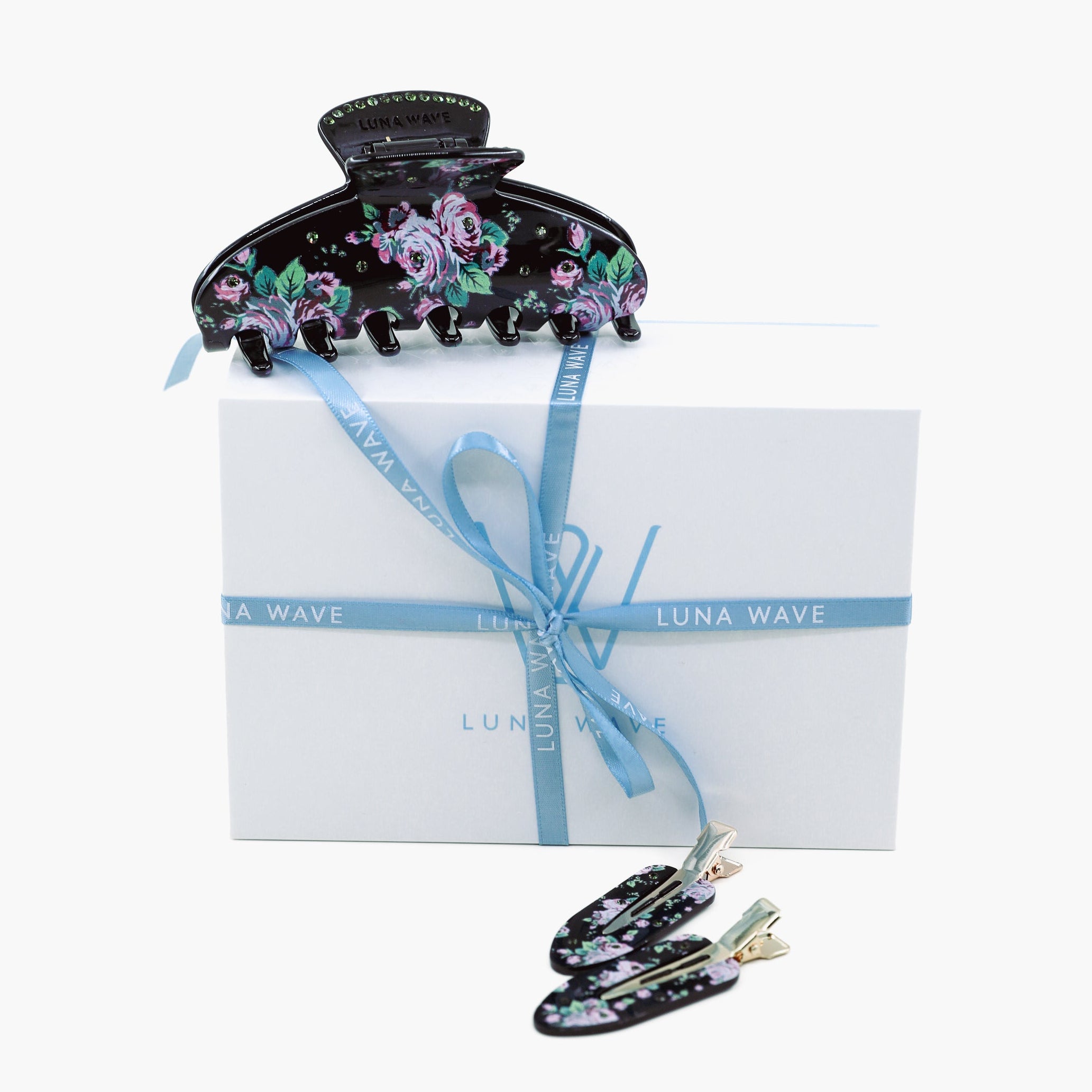 Black floral hair clip with a white box and blue ribbon on a white background
