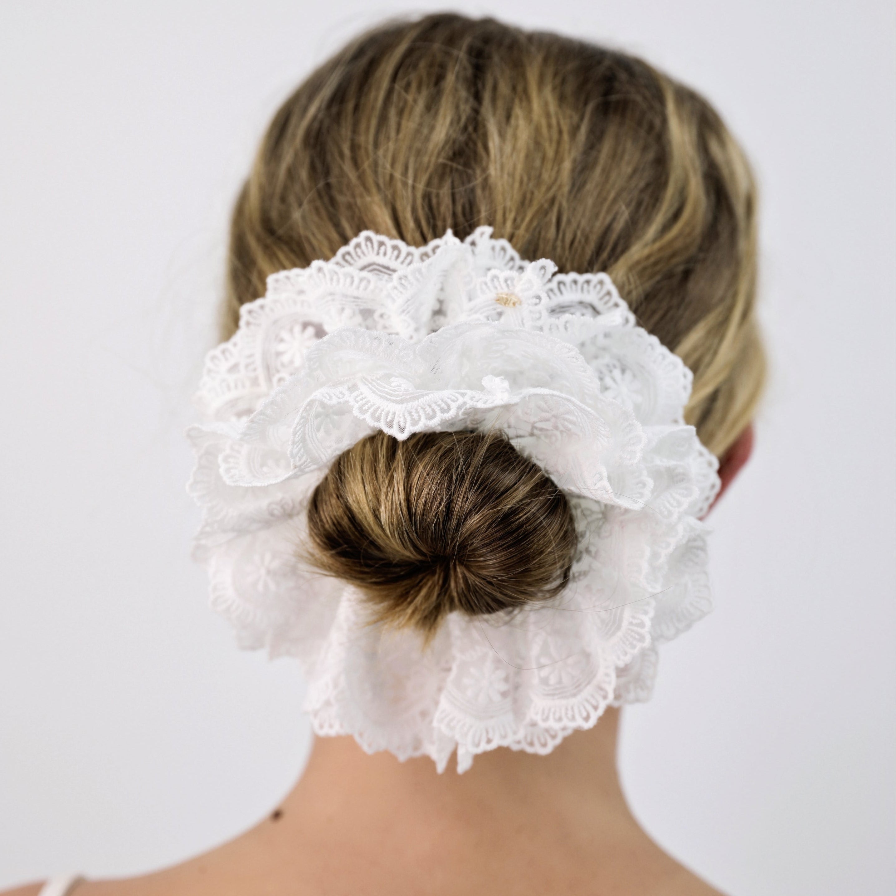 Woman with a bun covered by a Luna Wave white ivory lace hair accessory against a plain background