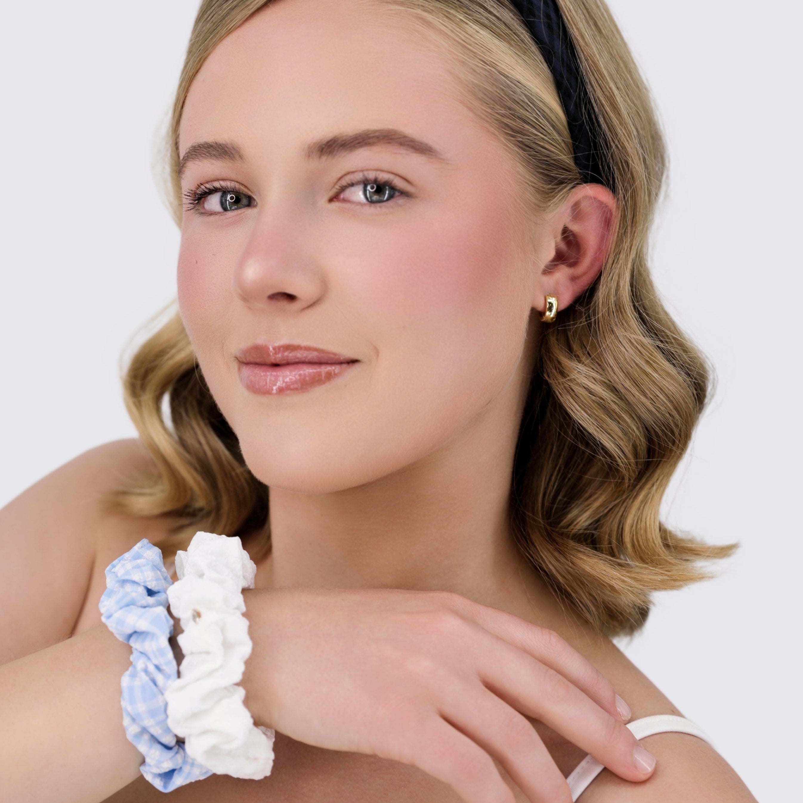 Woman wearing a Luna Wave gingham headband and white lace scrunchie on a plain background