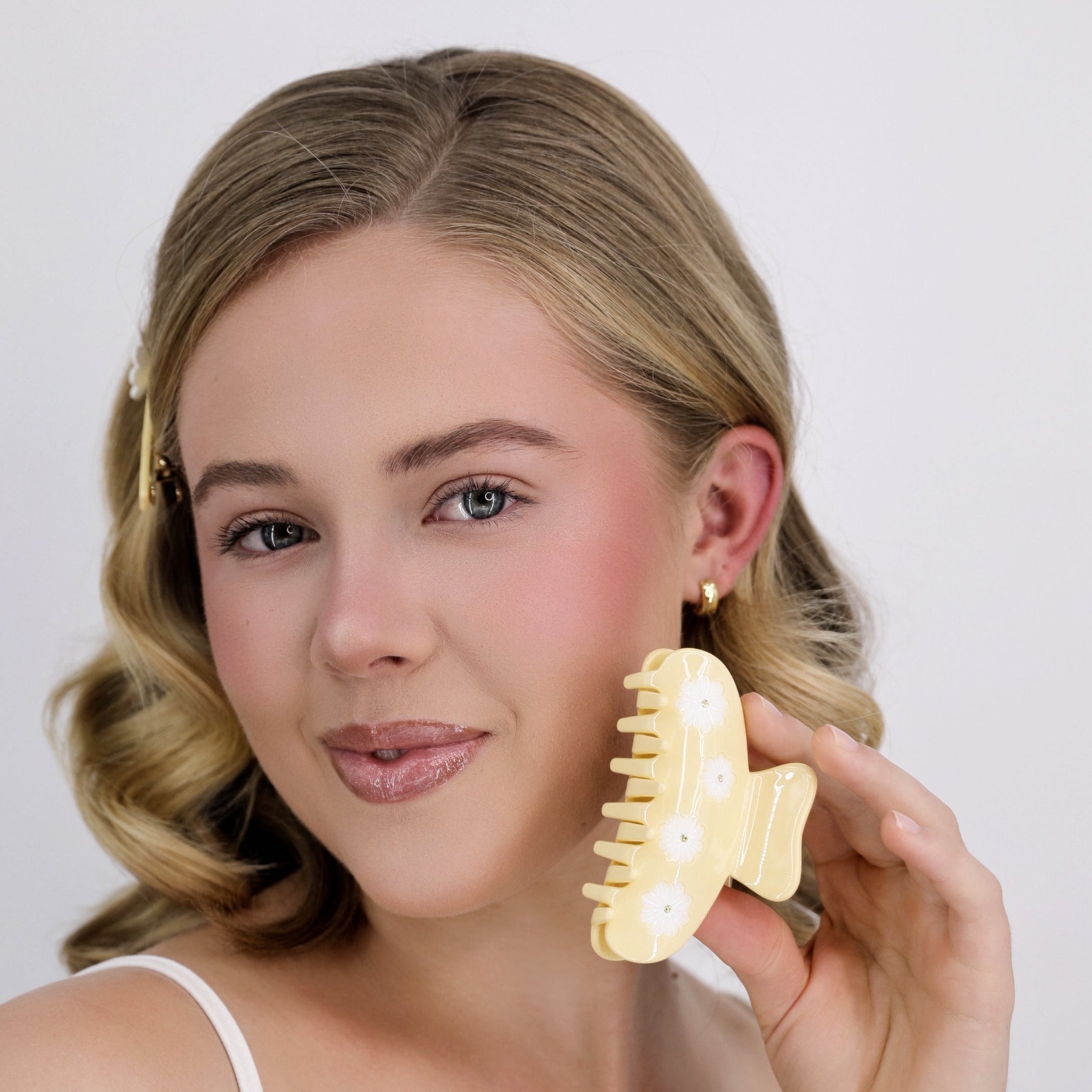 Woman holding a Luna Wave yellow daisy hair claw clip against a plain background
